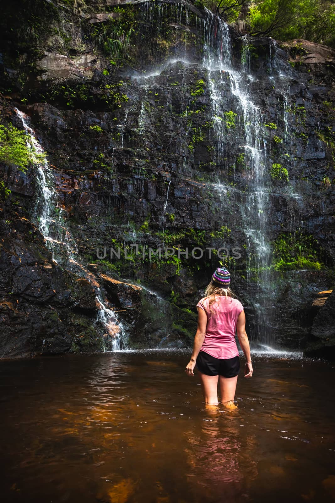 A female stands in the cooling waters of the rock pool after descending off the top of the mountain deep into the ravine  wilderness where this waterfall is located.