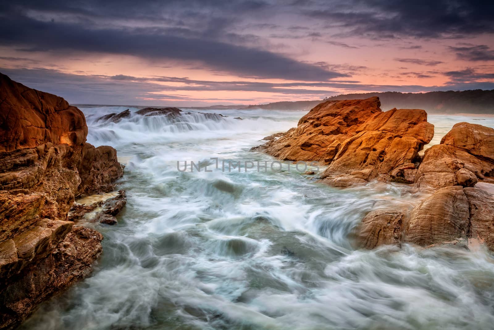 Bermagui rocky coastline a haven for fisherman and photographers who brave the conditions , views through the gully as waves cascade over rocks and surge forward with the incoming tide.