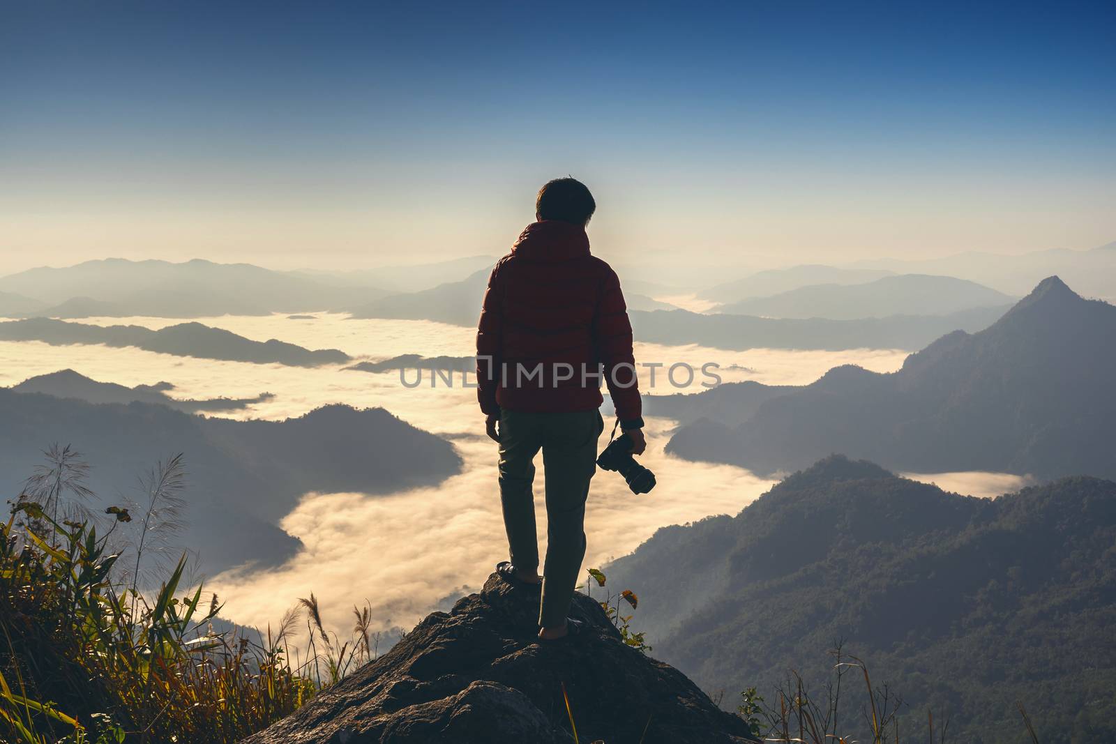 Photographer hand holding camera and standing on top of the rock in nature. Travel concept.