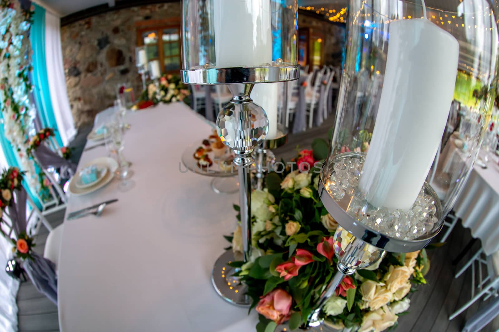 Table decoration for wedding reception. Candlestick with candles and bouquet of flowers on wedding table setting with white tablecloth. Shot with fisheye lens. 