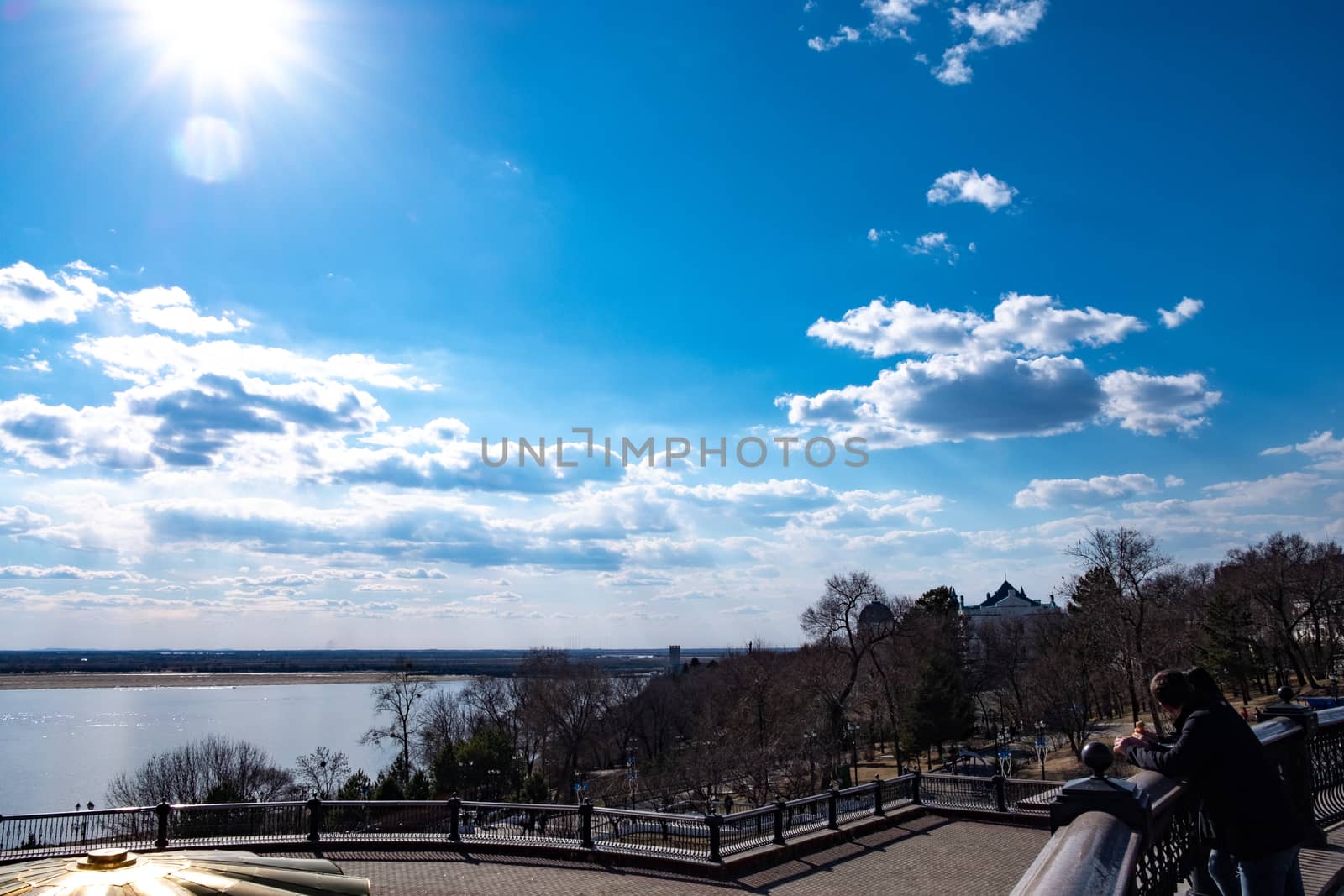 The spring Park is illuminated by the bright sun. View of a large and powerful river. On the bright blue sky beautiful white clouds.