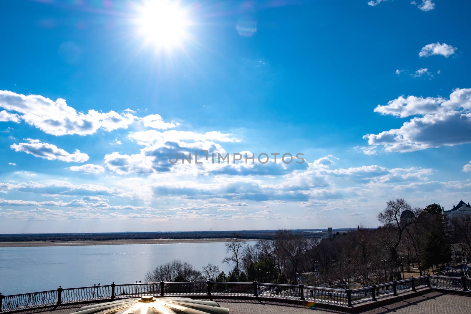 The spring Park is illuminated by the bright sun. View of a large and powerful river. On the bright blue sky beautiful white clouds.