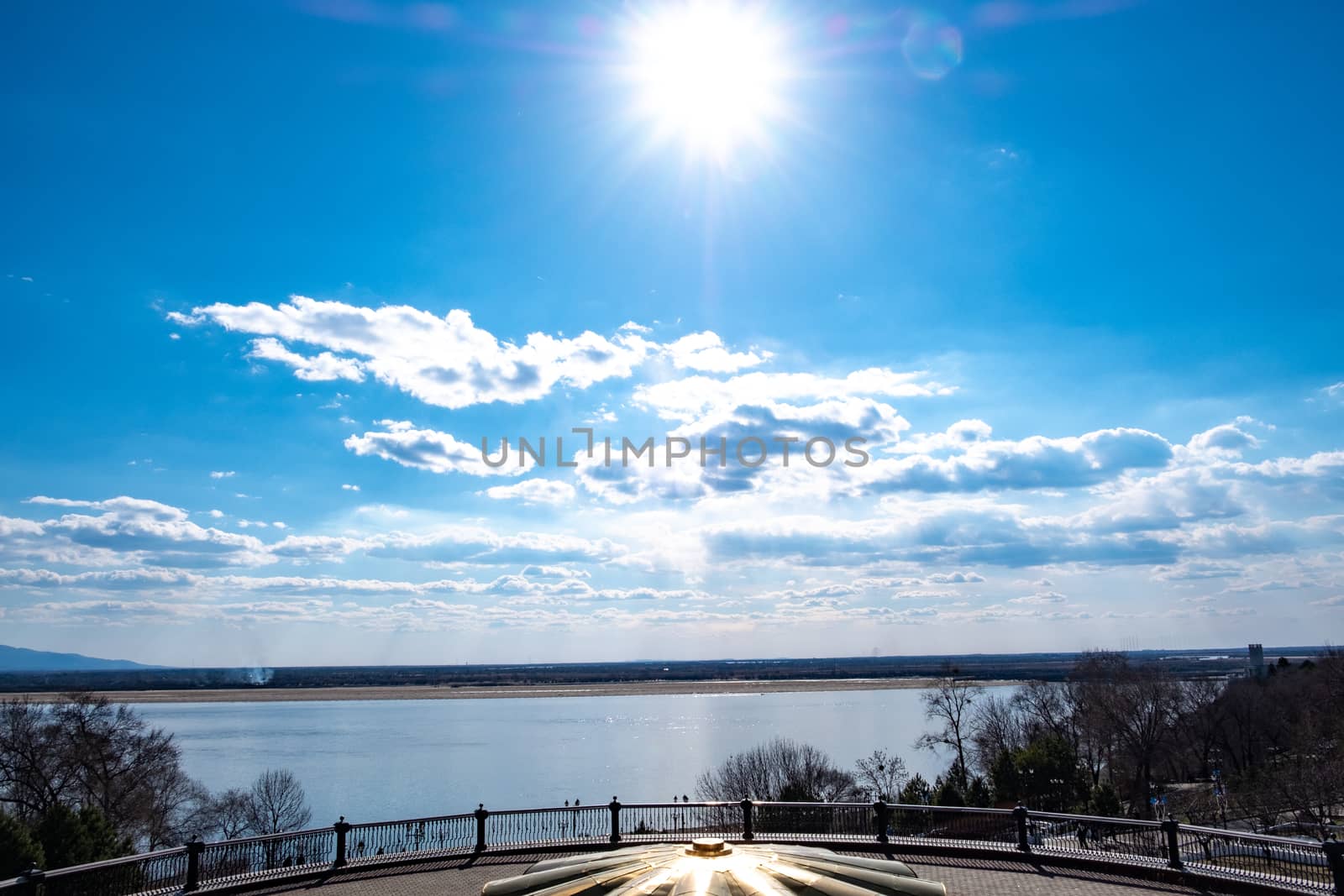 The spring Park is illuminated by the bright sun. View of a large and powerful river. On the bright blue sky beautiful white clouds.