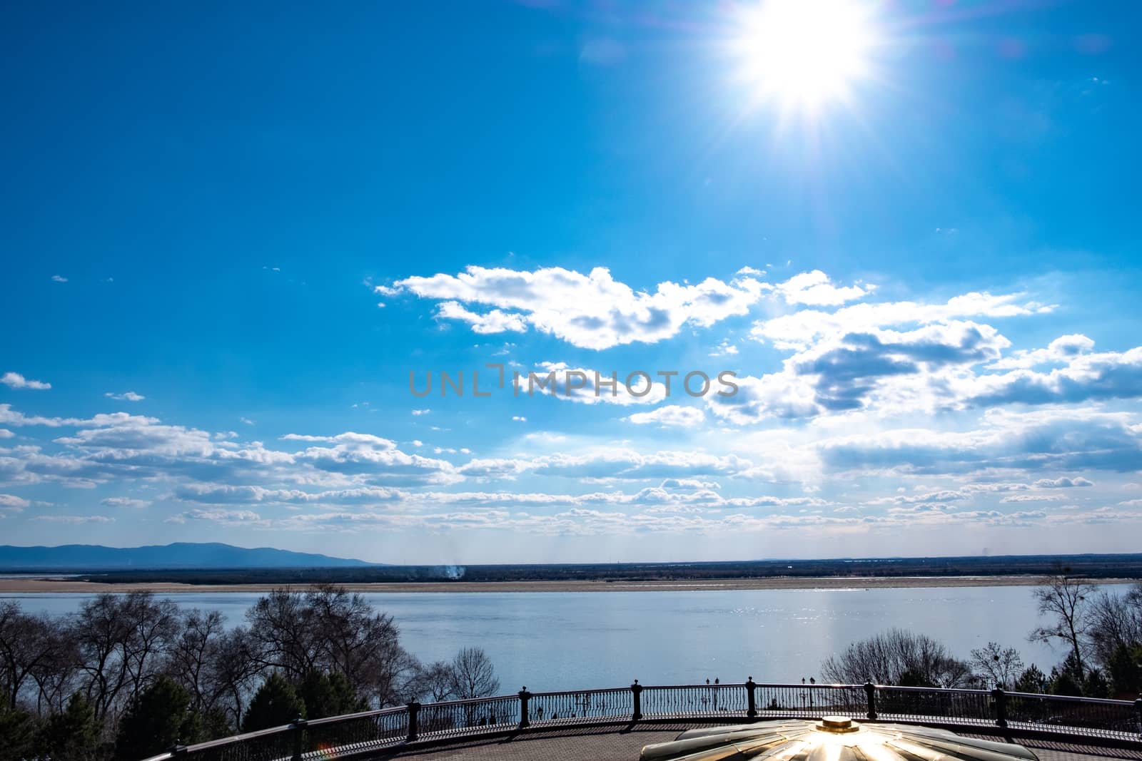 The spring Park is illuminated by the bright sun. View of a large and powerful river. On the bright blue sky beautiful white clouds.