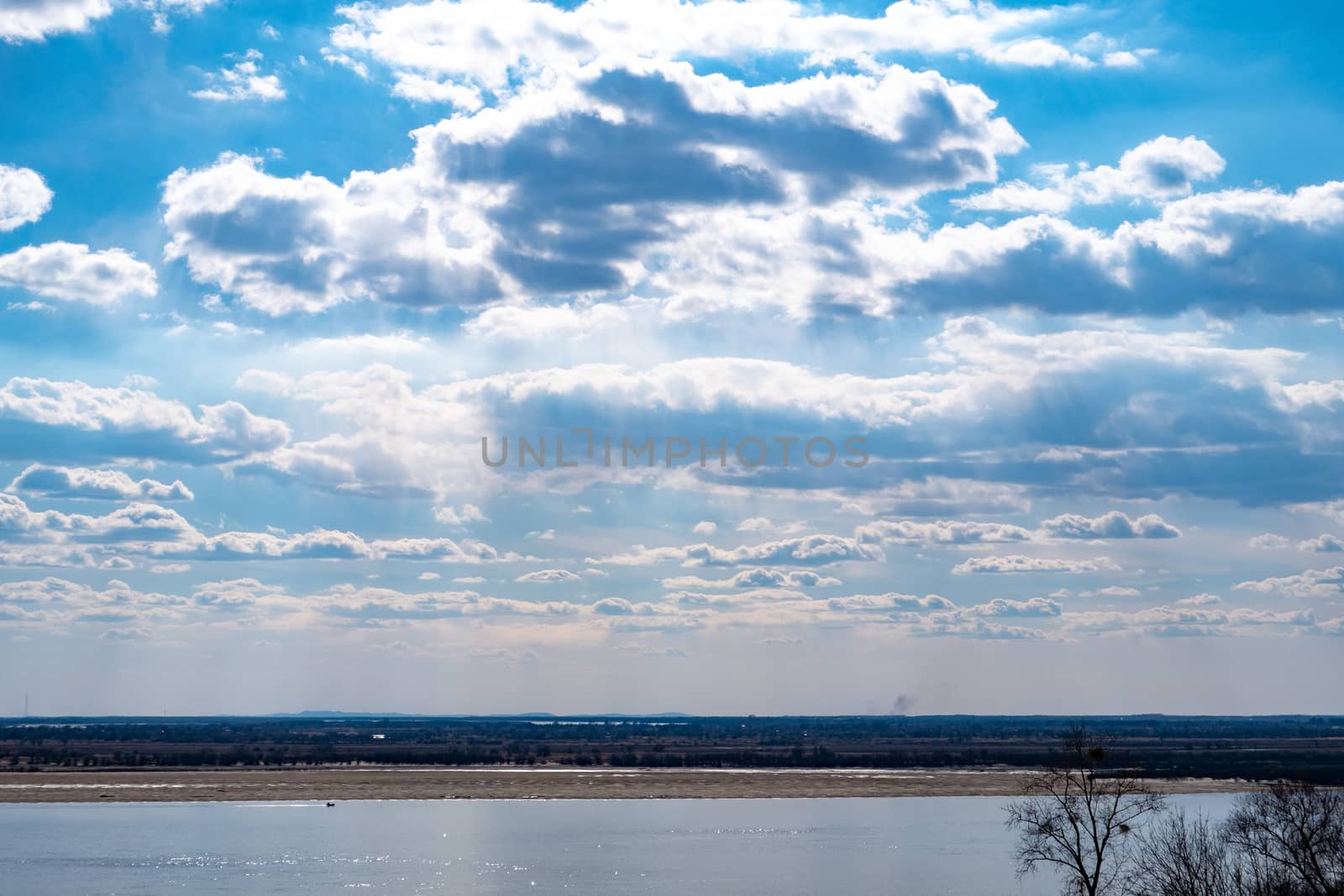 The spring Park is illuminated by the bright sun. View of a large and powerful river. On the bright blue sky beautiful white clouds.