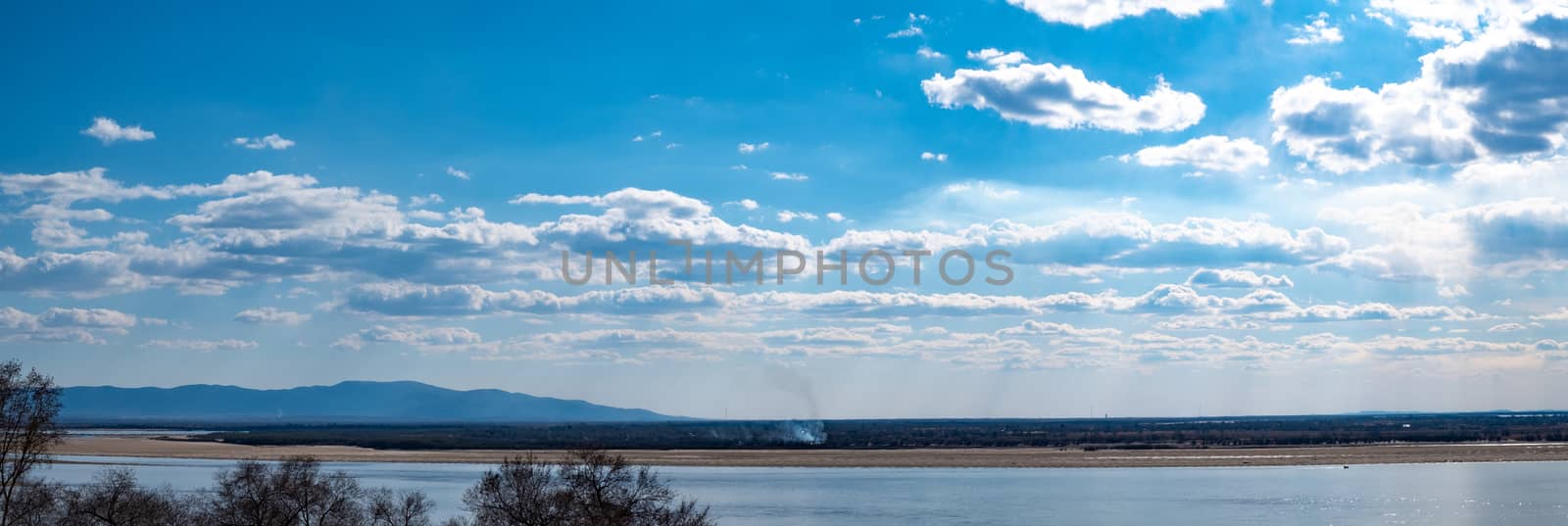 The spring Park is illuminated by the bright sun. View of a large and powerful river. On the bright blue sky beautiful white clouds.