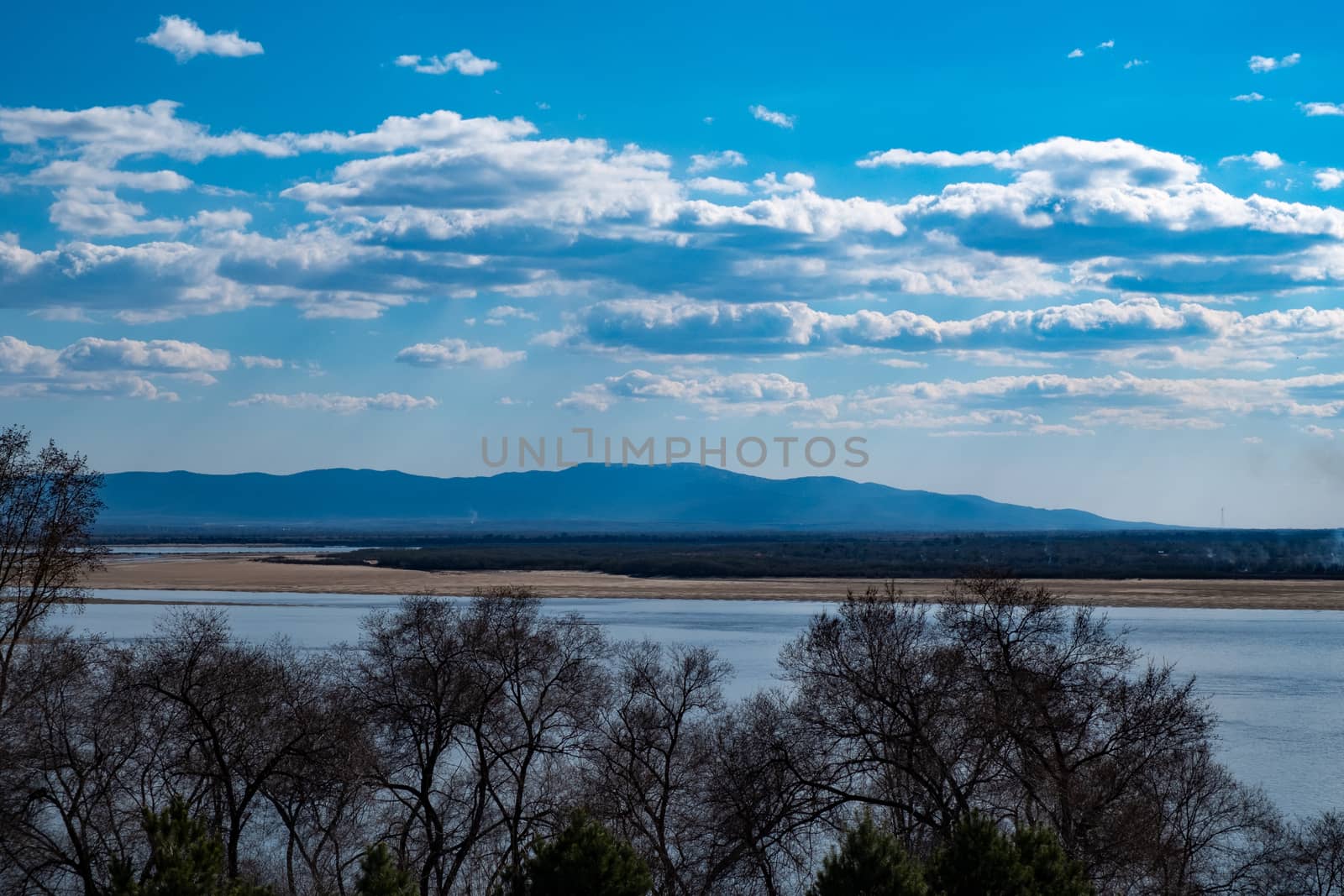 The spring Park is illuminated by the bright sun. View of a large and powerful river. On the bright blue sky beautiful white clouds.