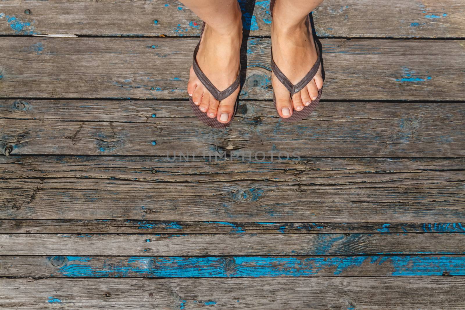 Top view, photo of female legs in beach flip flops on a wooden old floor. Photos on vacation, beach, summer.