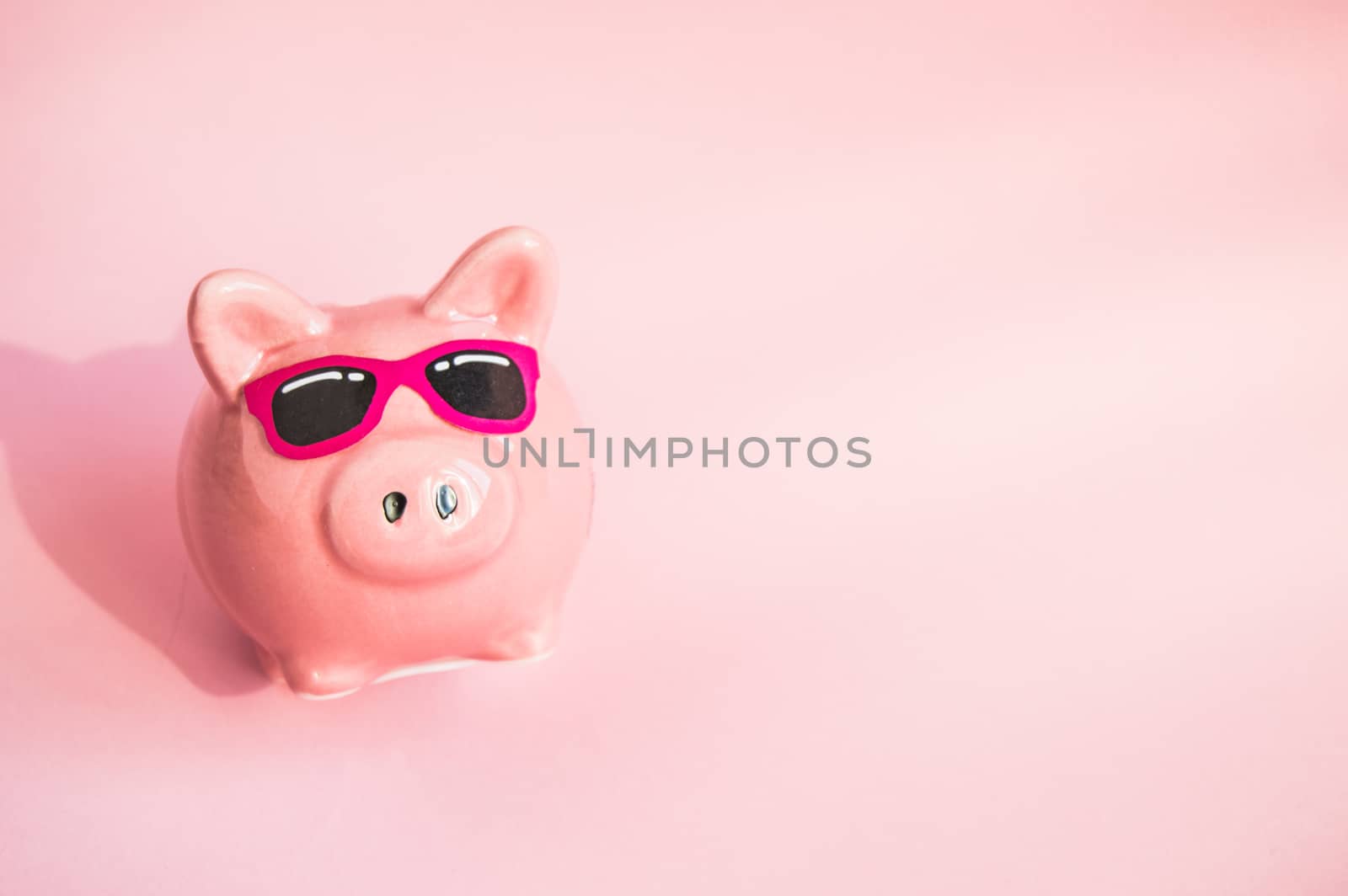 Funny piggy Bank in sunglasses on pink background, sunlight, copy space, money saving concept for summer vacation.