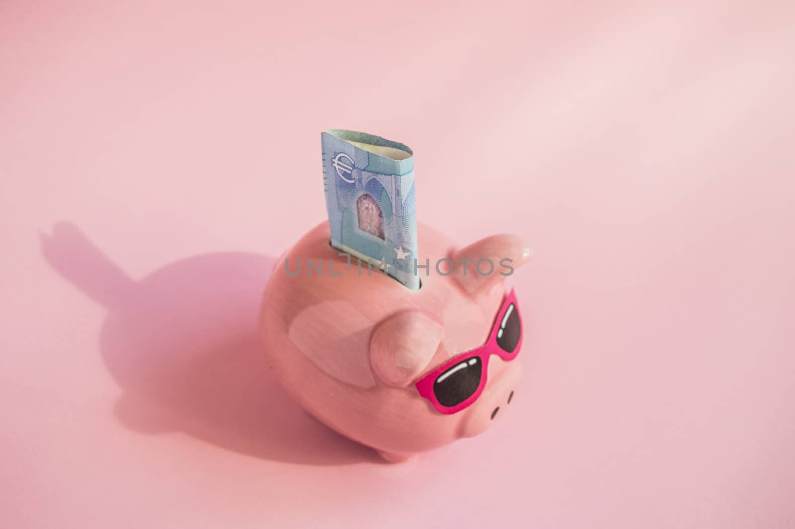Concept of saving money on your trip or vacation pig piggy Bank with sunglasses on the bill of euros on a pink background, place for text.