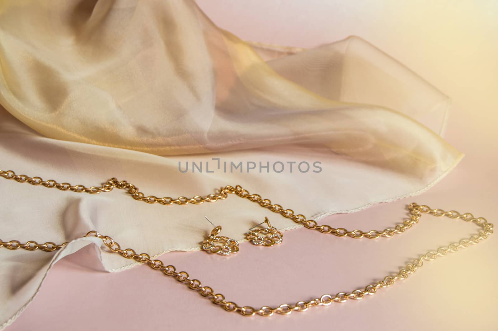Luxury gold jewelry chain and earrings on pink background with silk, copy space, selective focus by claire_lucia