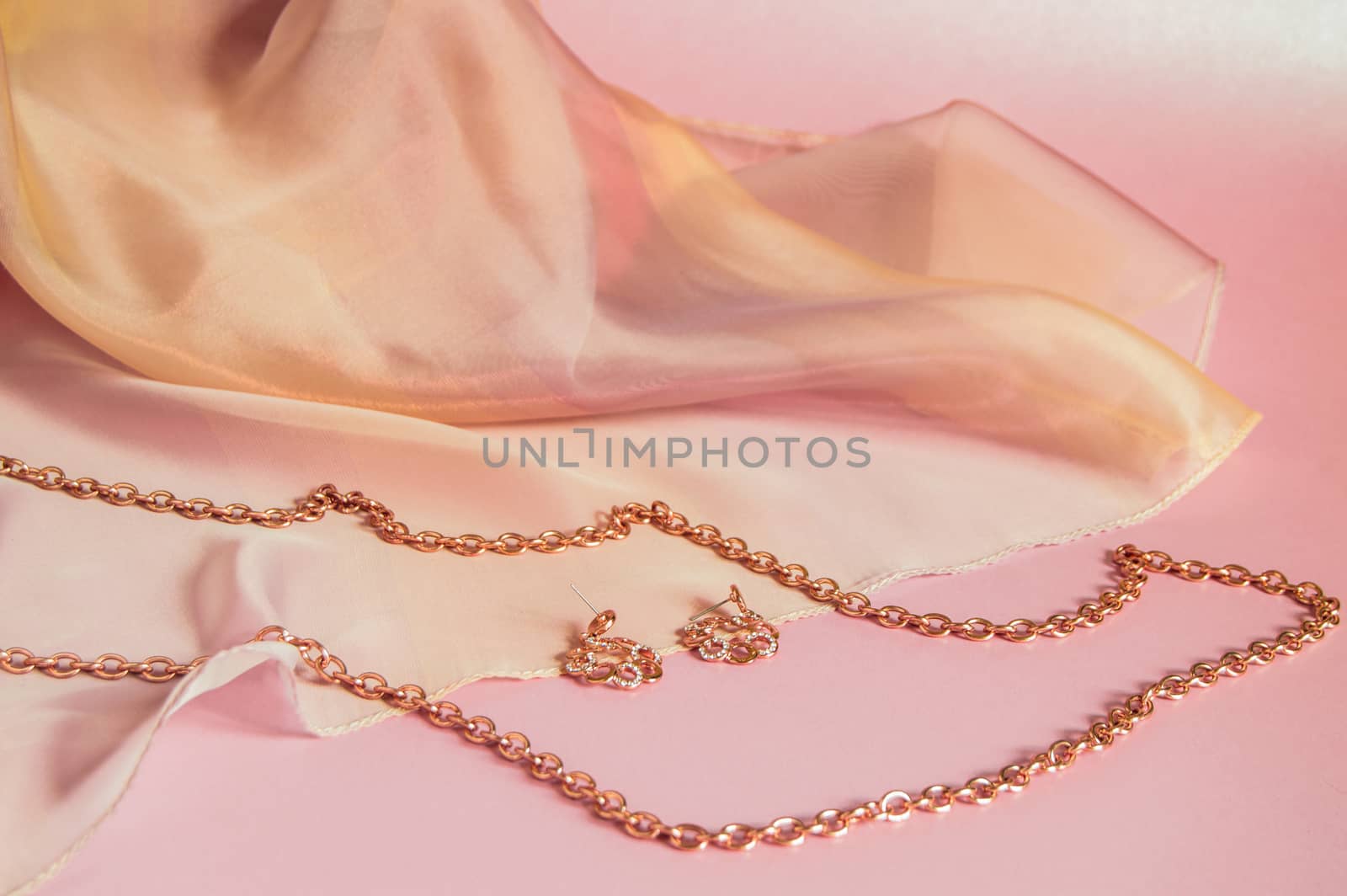 Luxury gold jewelry chain and earrings on pink background with silk, copy space, selective focus.