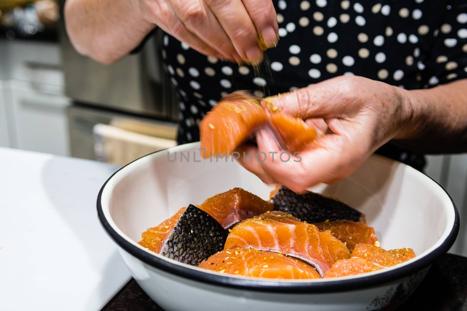 The cook pours spices into fish before putting them in the oven.