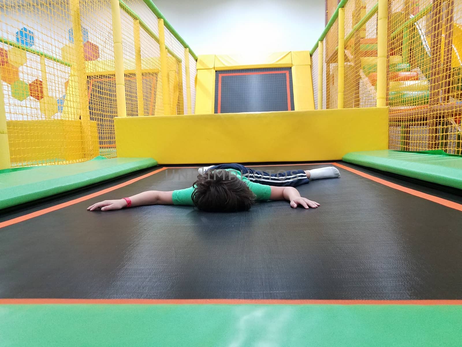 exhausted boy child laying down on green and yellow trampoline by stockphotofan1