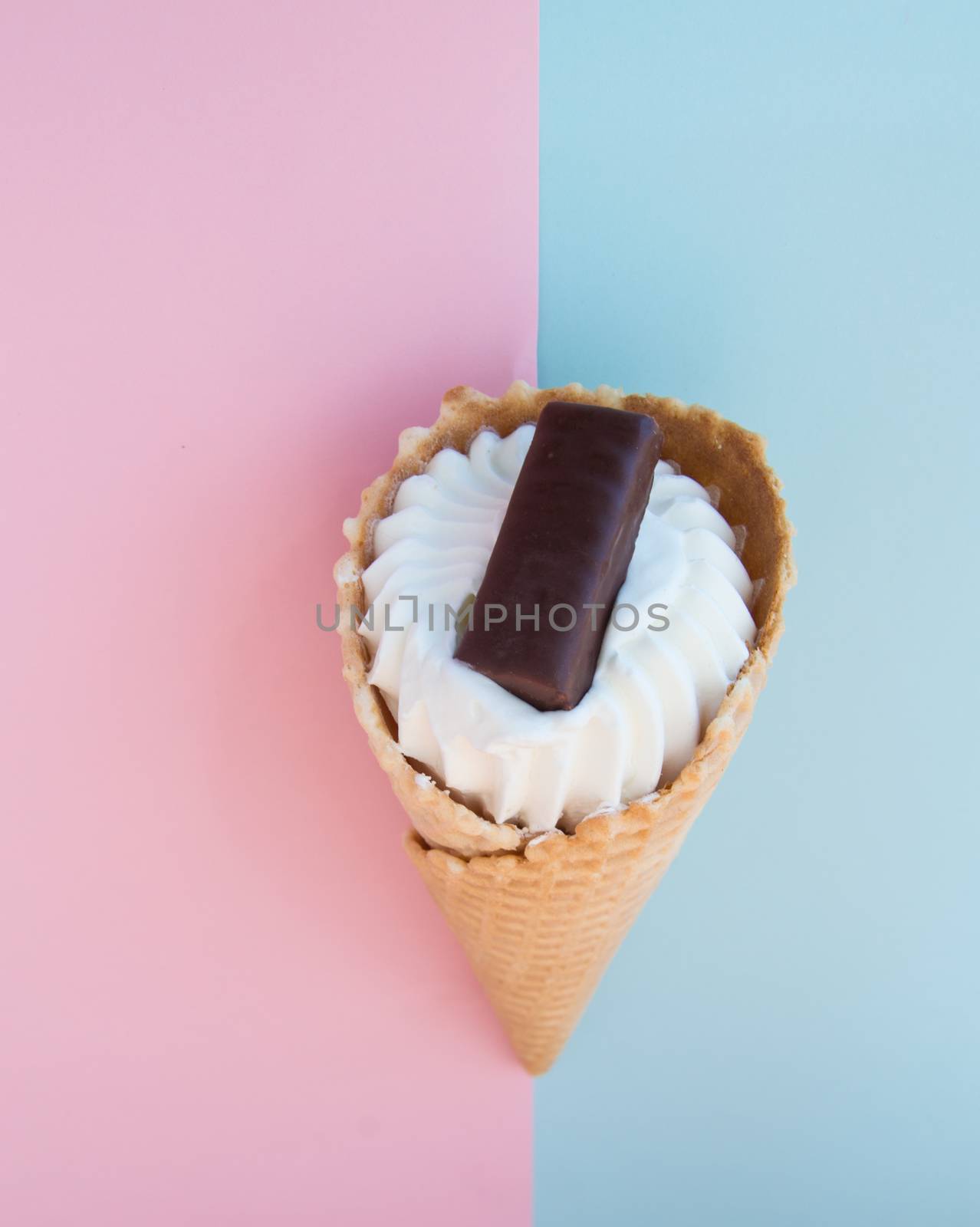 Vanilla ice cream cone with chocolate on a background of pastel colors pink and blue, top view.
