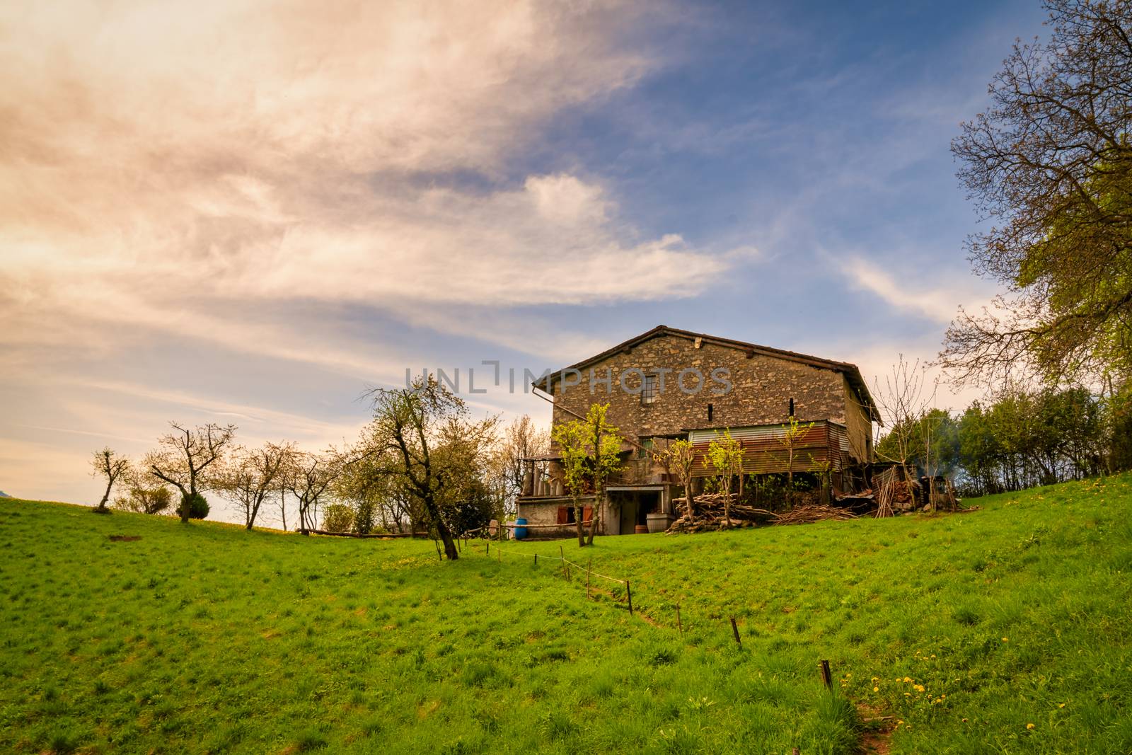 Panorama of green hills in Orobie mountains with typical mountain house built in stone.