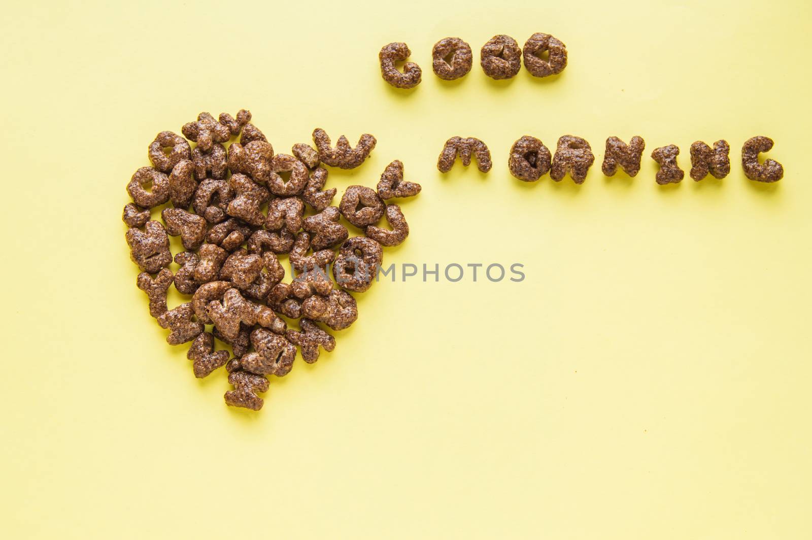 Heart sign on the table and the inscription Good morning, made of dry Breakfast - chocolate flakes in the form of letters of the alphabet, yellow background, top view