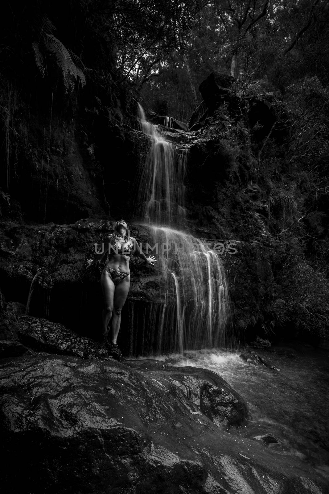 A shimmering waterfall rushed over her.  Standing on slippery rocks wet from the cascades the woman let the falling water invigorate herskin before taking a swim in a secluded waterhole in bushland Australia