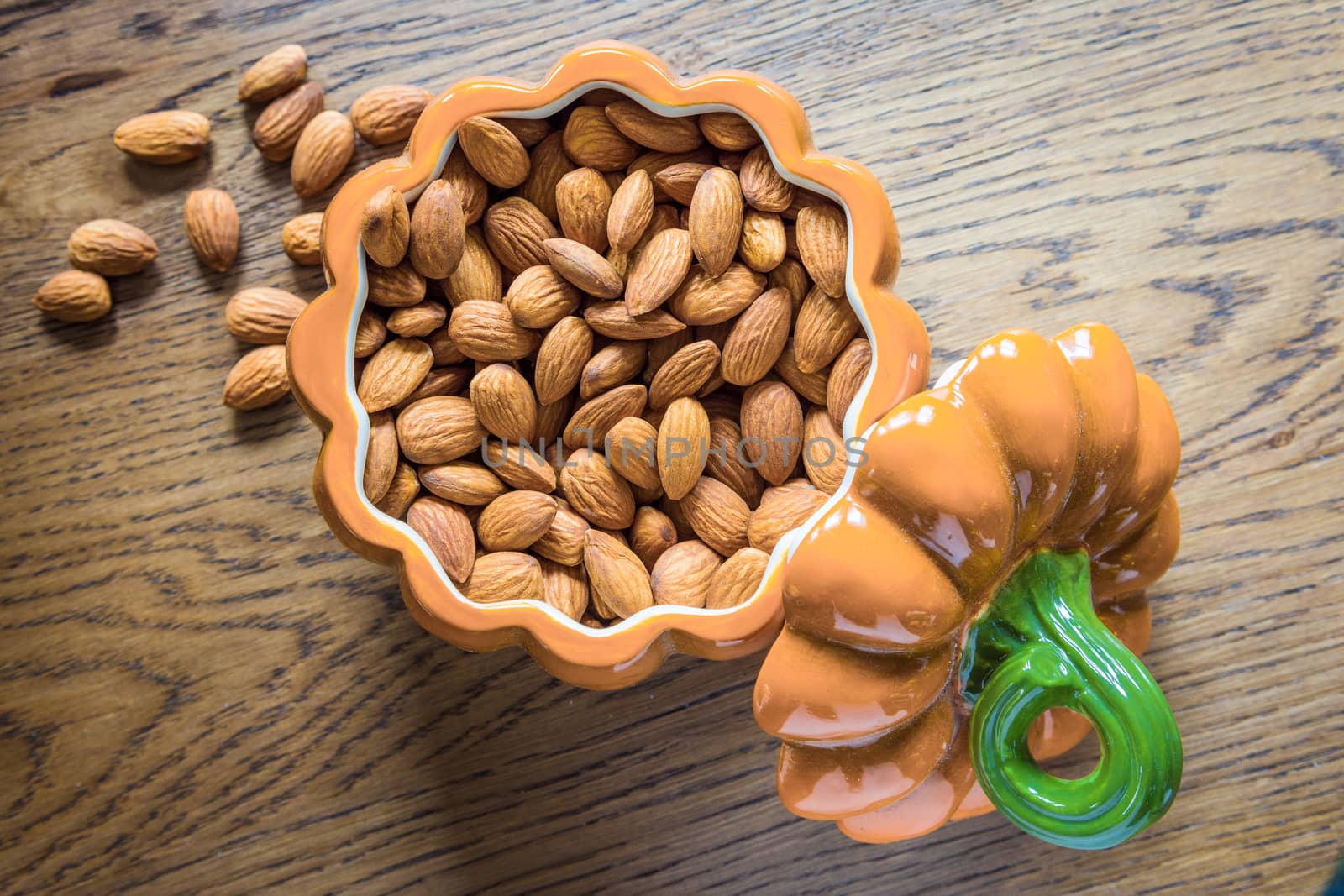 Almond nuts lie in an open ceramic bowl made in the shape of a pumpkin. 
