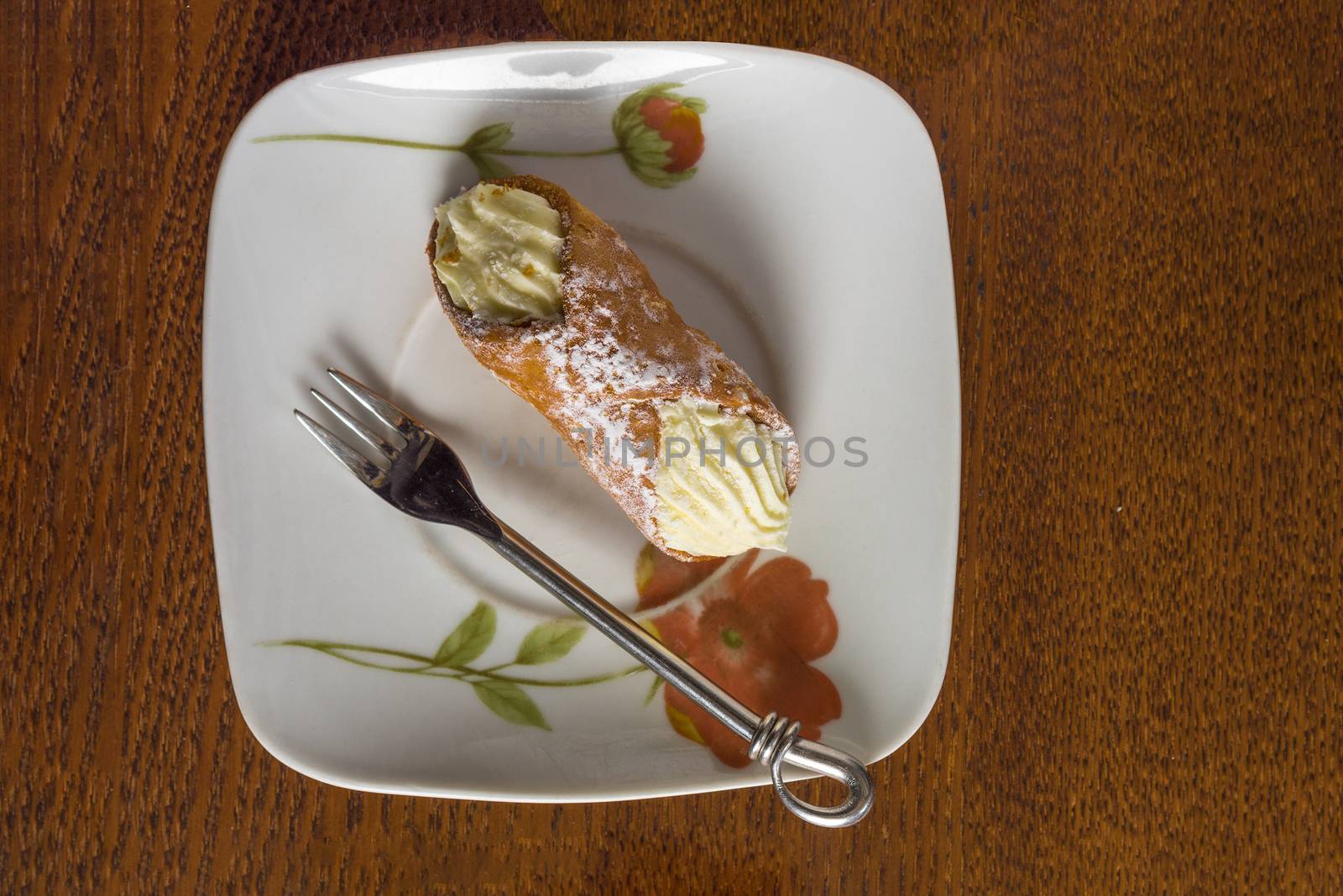 Canoli cake and a triple fork lie on a square, ceramic plate.