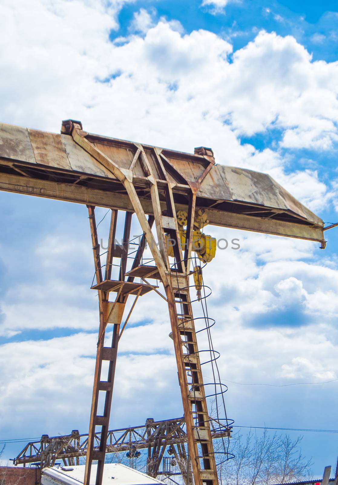 Old rusty gantry crane on blue sky background, vertical shot, outdoors.