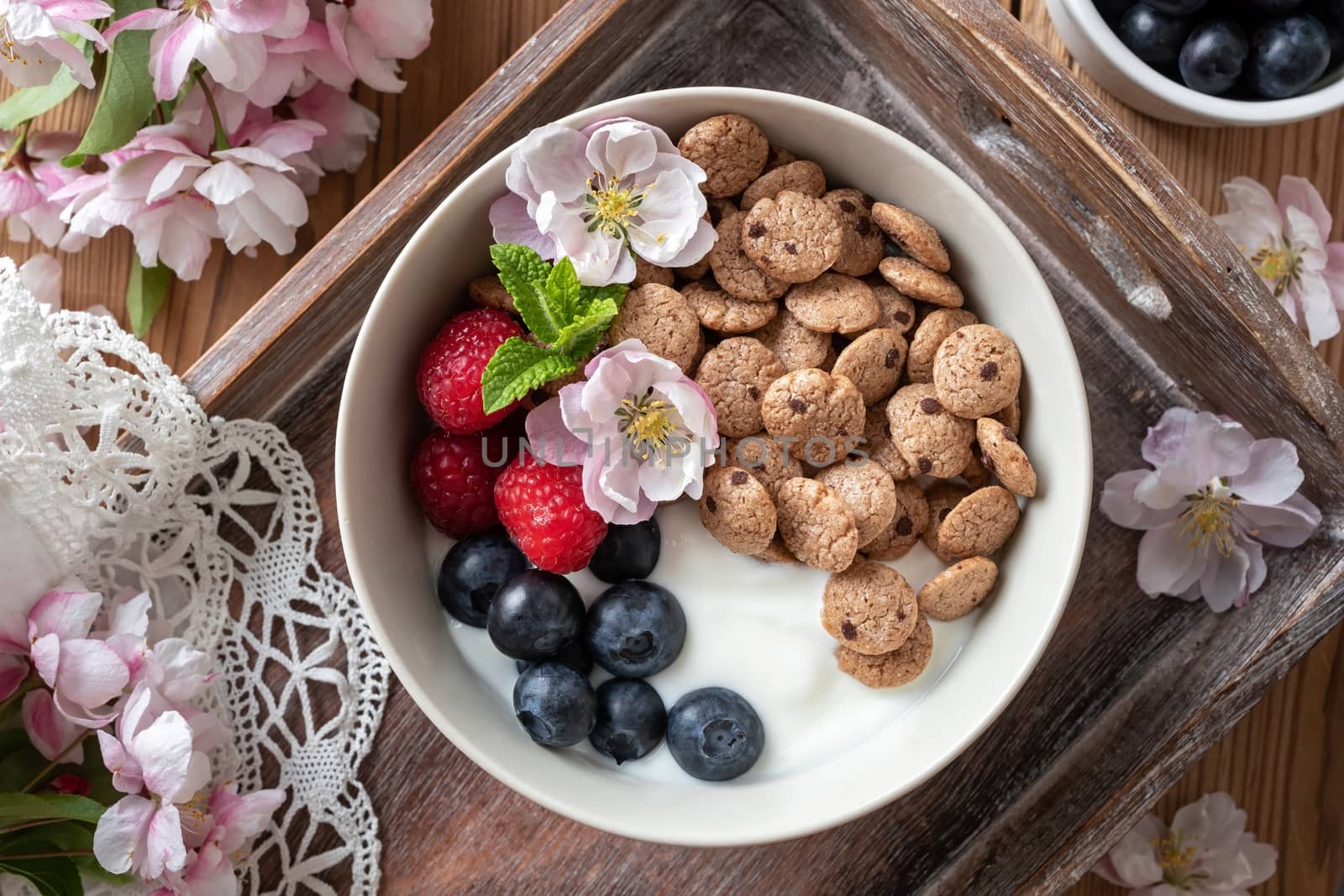 Breakfast cereals with yogurt, blueberries, raspberries and spring blossoms on a rustic background