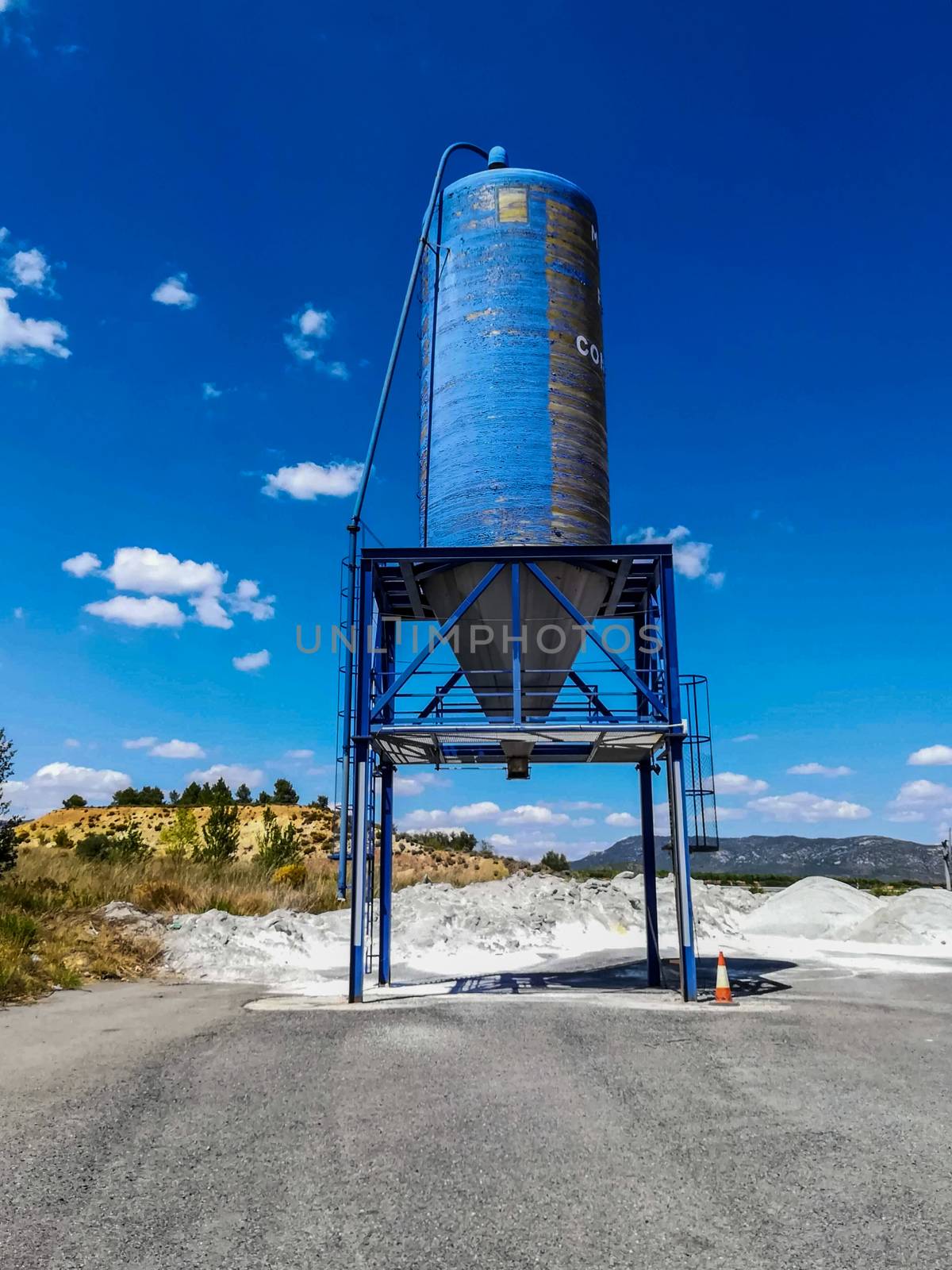 Blue silo of white cement on a mountain with little vegetation and blue sky