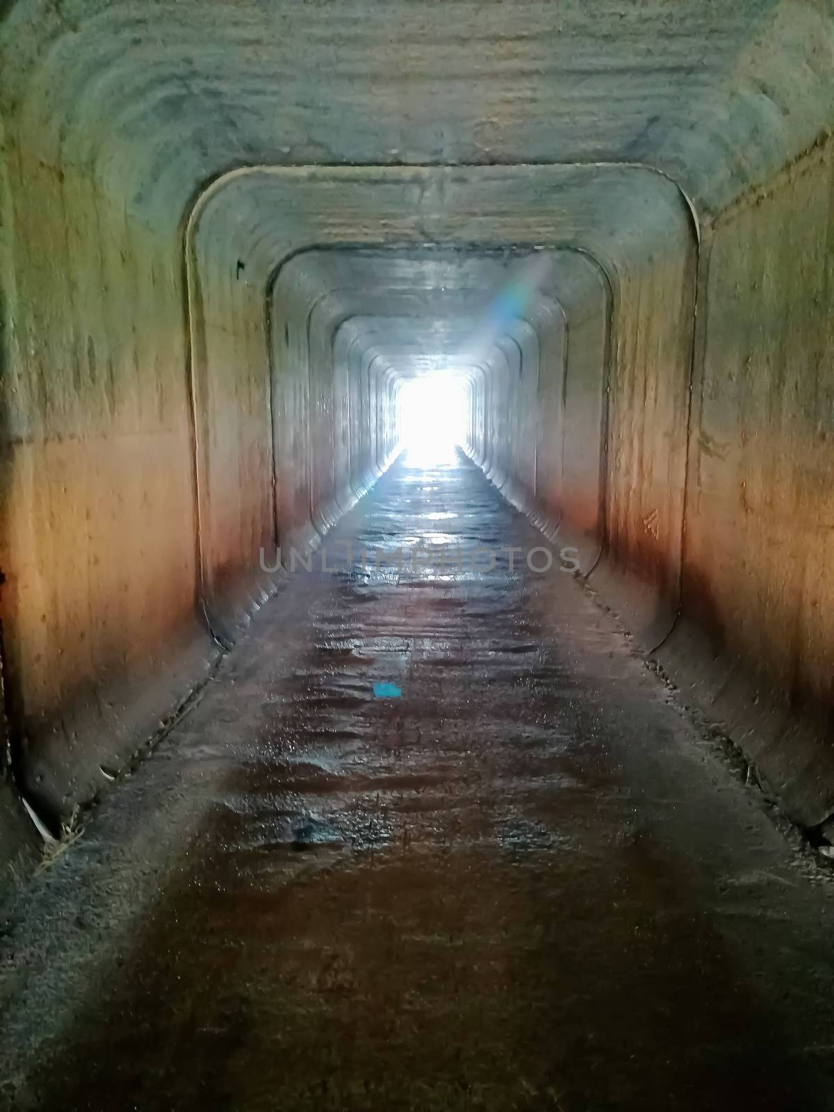 Square tunnel passing under a highway with sunlight entering at the end of the tunnel
