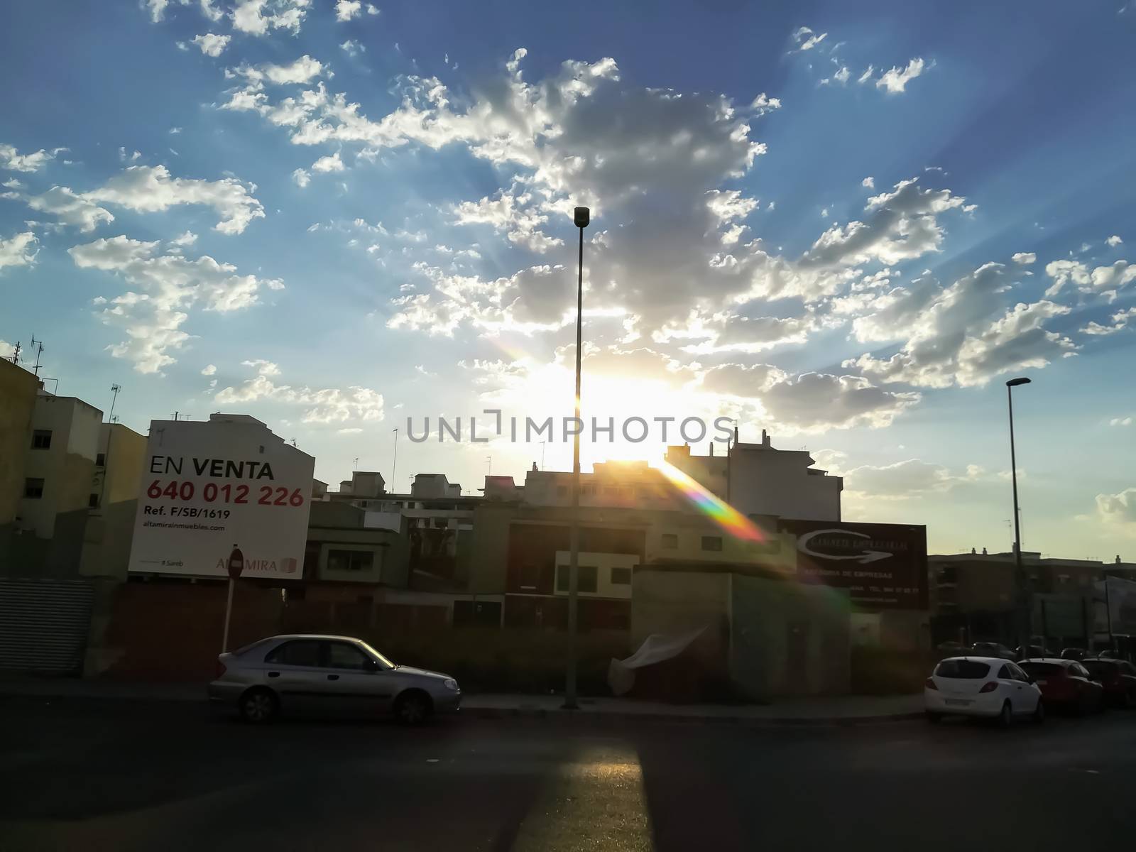 Sun peeping above the buildings with clouds in the blue sky