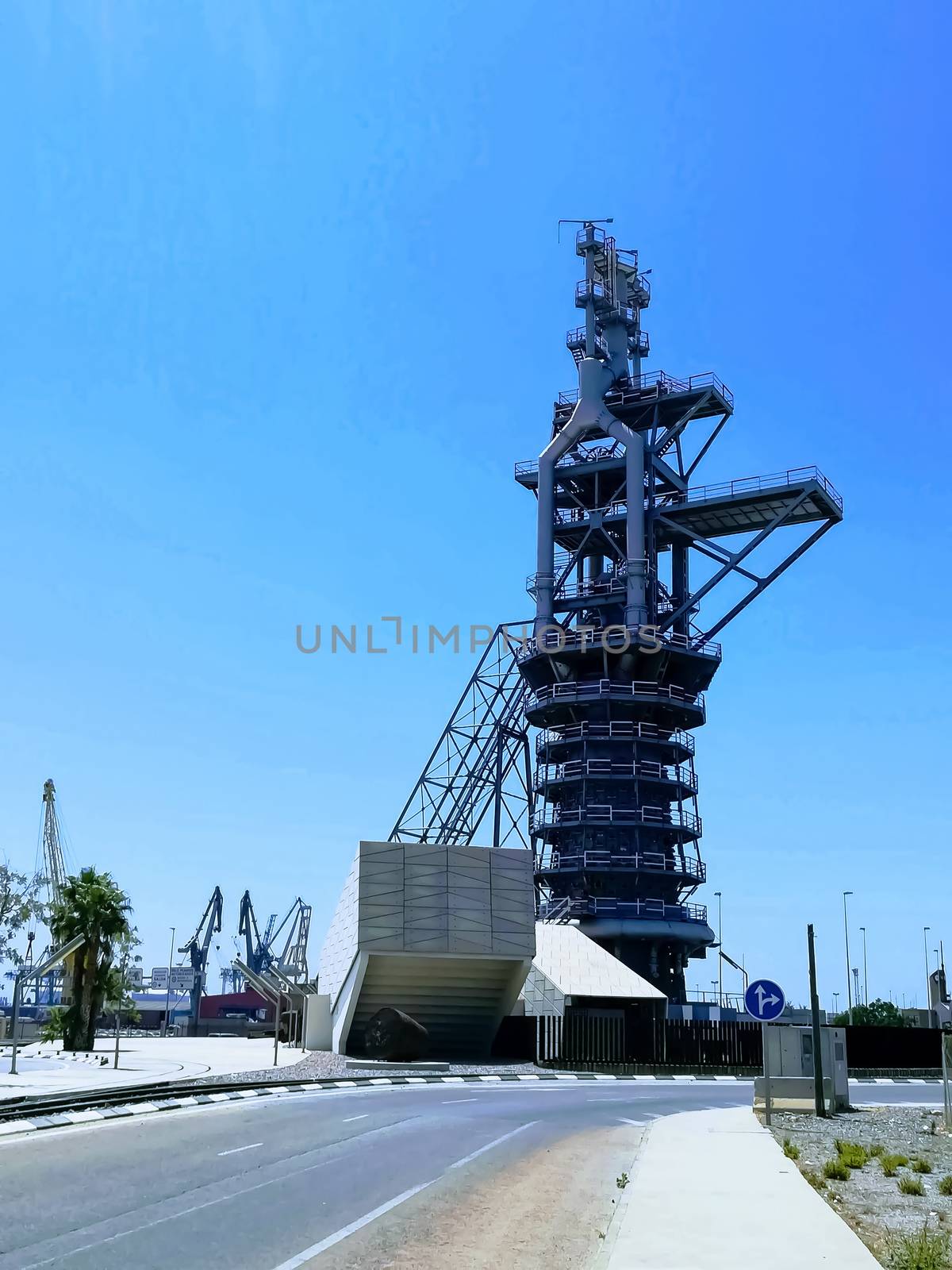 View of the old blast furnace exposed at a roundabout in the Port of Sagunto with the cranes of the commercial port in the background