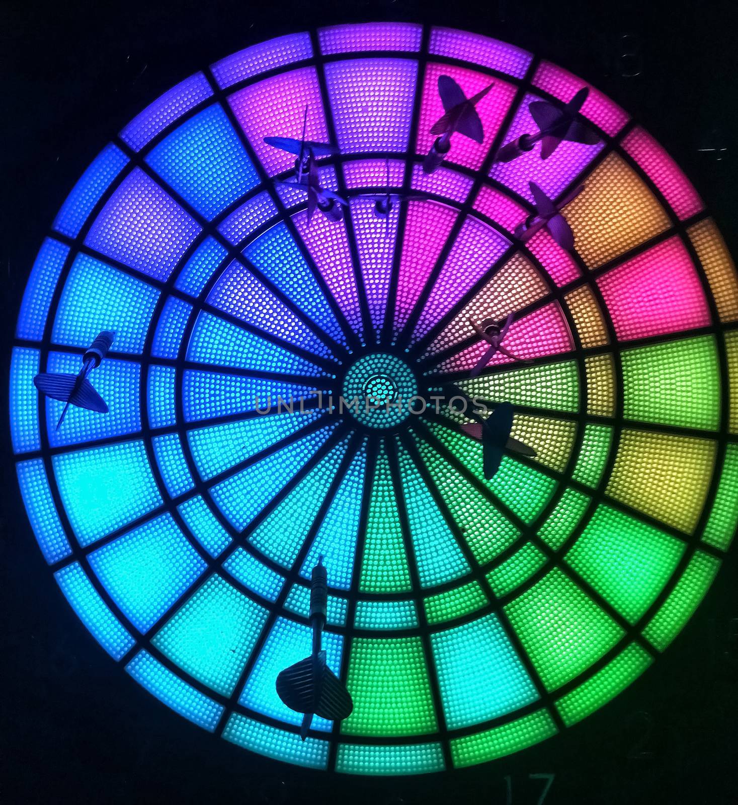 Luminous multicolored dartboard with several black darts nailed