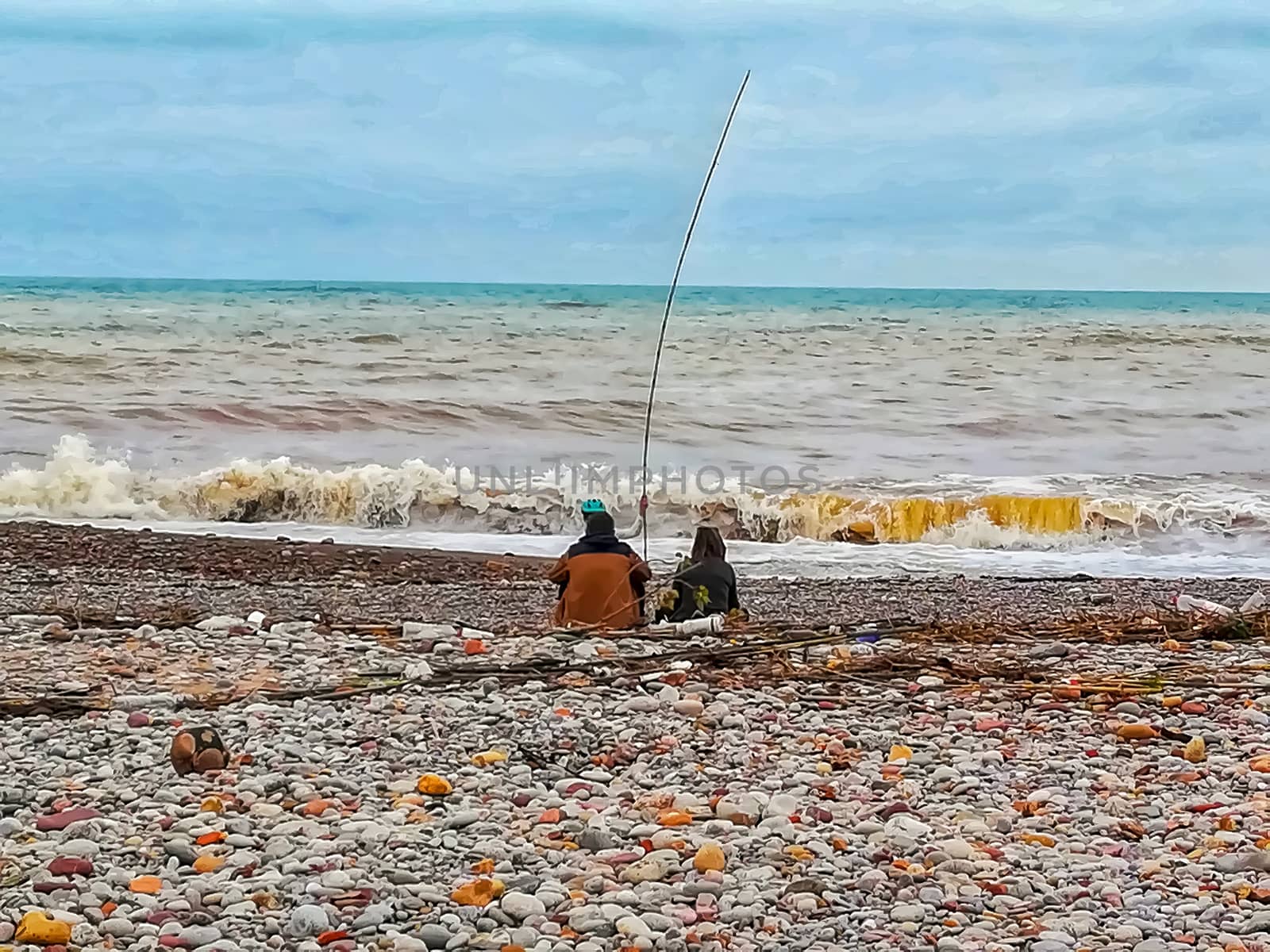People fishing on pebble beach with scrambled Mediterranean sea