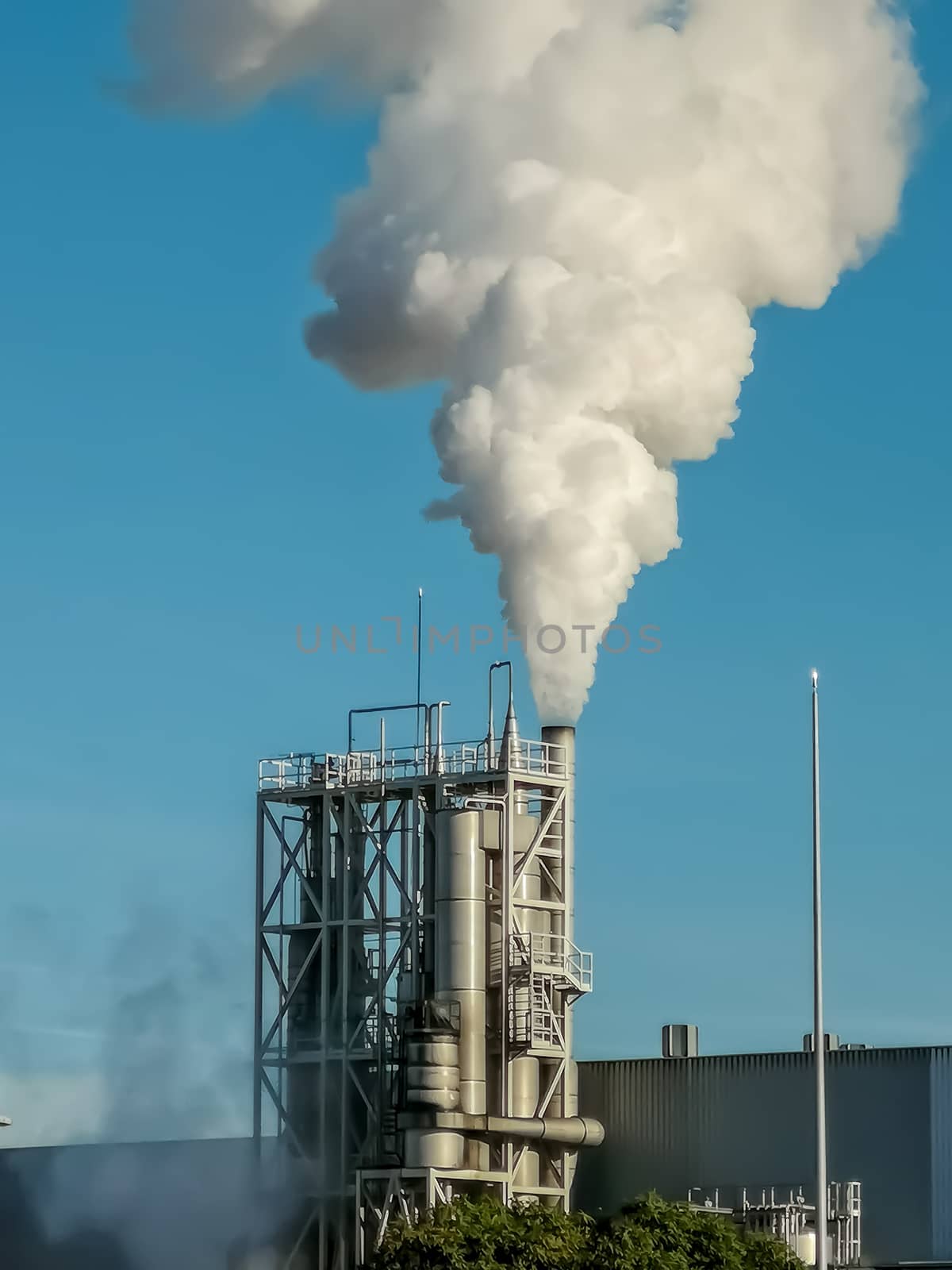 Industrial chimney expelling a lot of smoke over blue sky