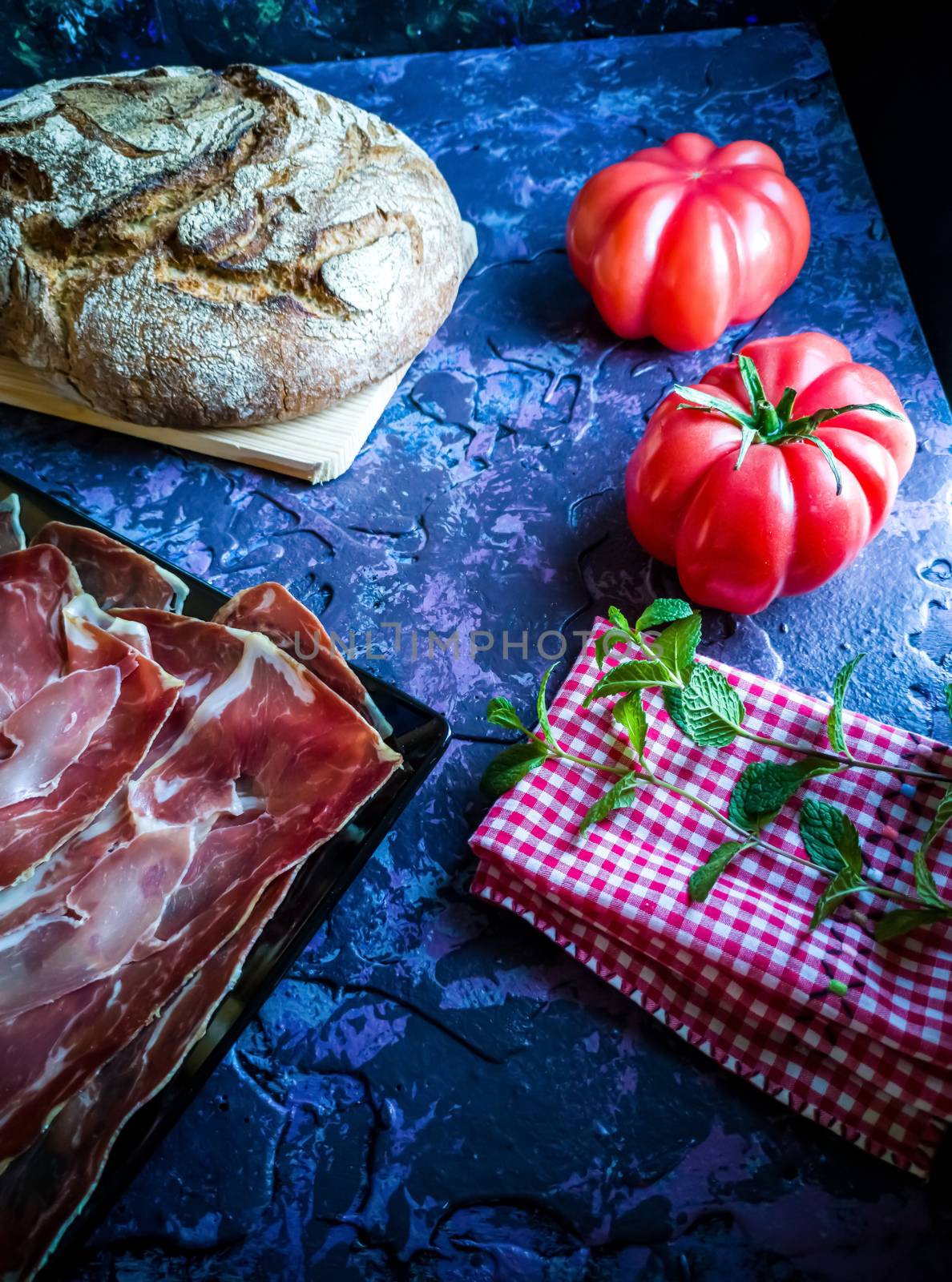 Ham, tomato, bread and herbs in composition on dark background with rough texture