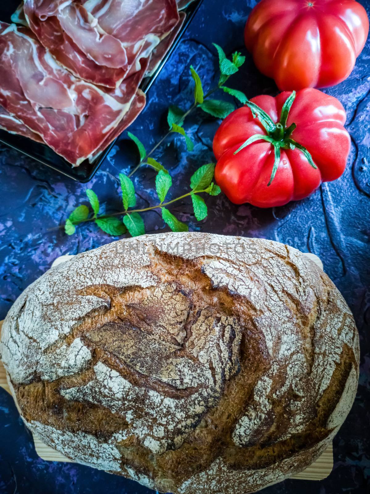 Ham, tomato, bread and herbs in composition on dark background with rough texture