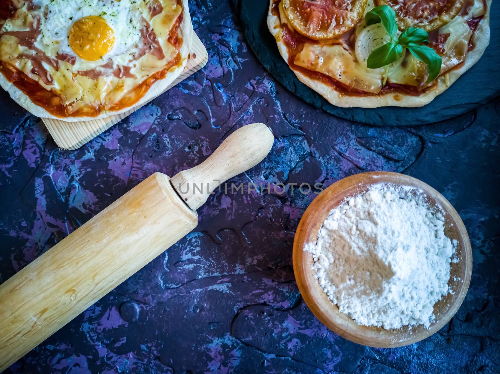 Homemade pizzas and utensils on dark background in lilac tones