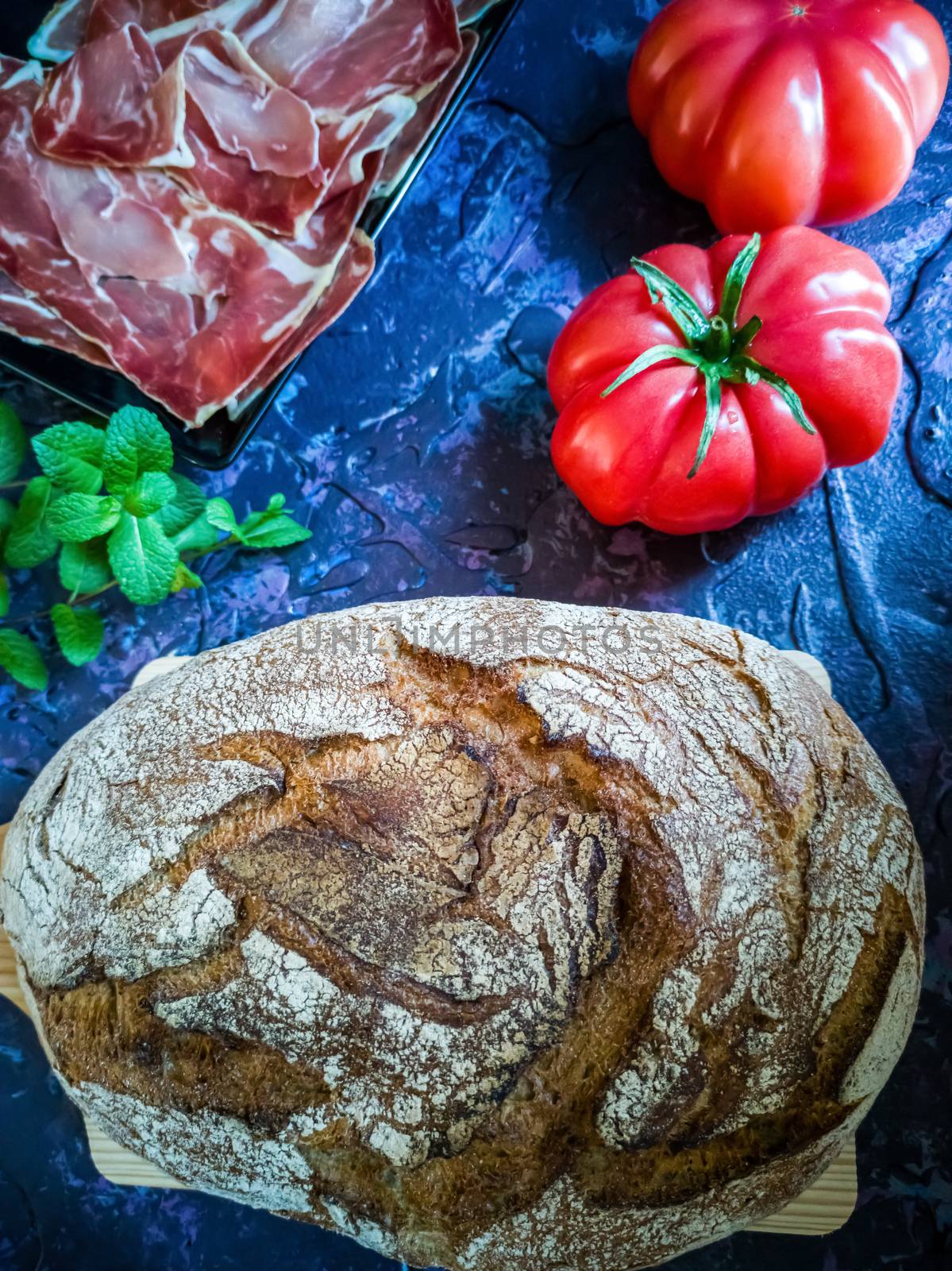 Ham, tomato, bread and herbs in composition on dark background with rough texture