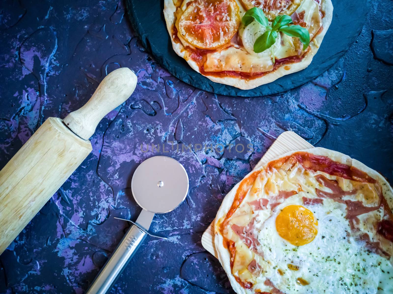 Homemade pizzas and utensils on dark background in lilac tones