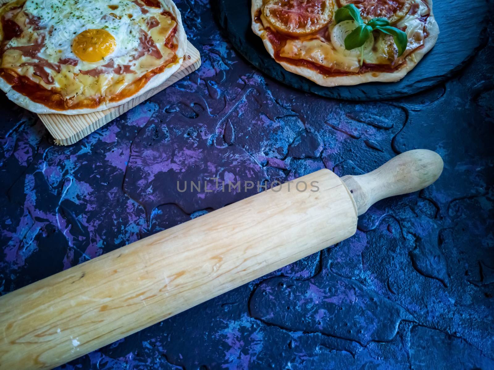 Homemade pizzas and utensils on dark background in lilac tones