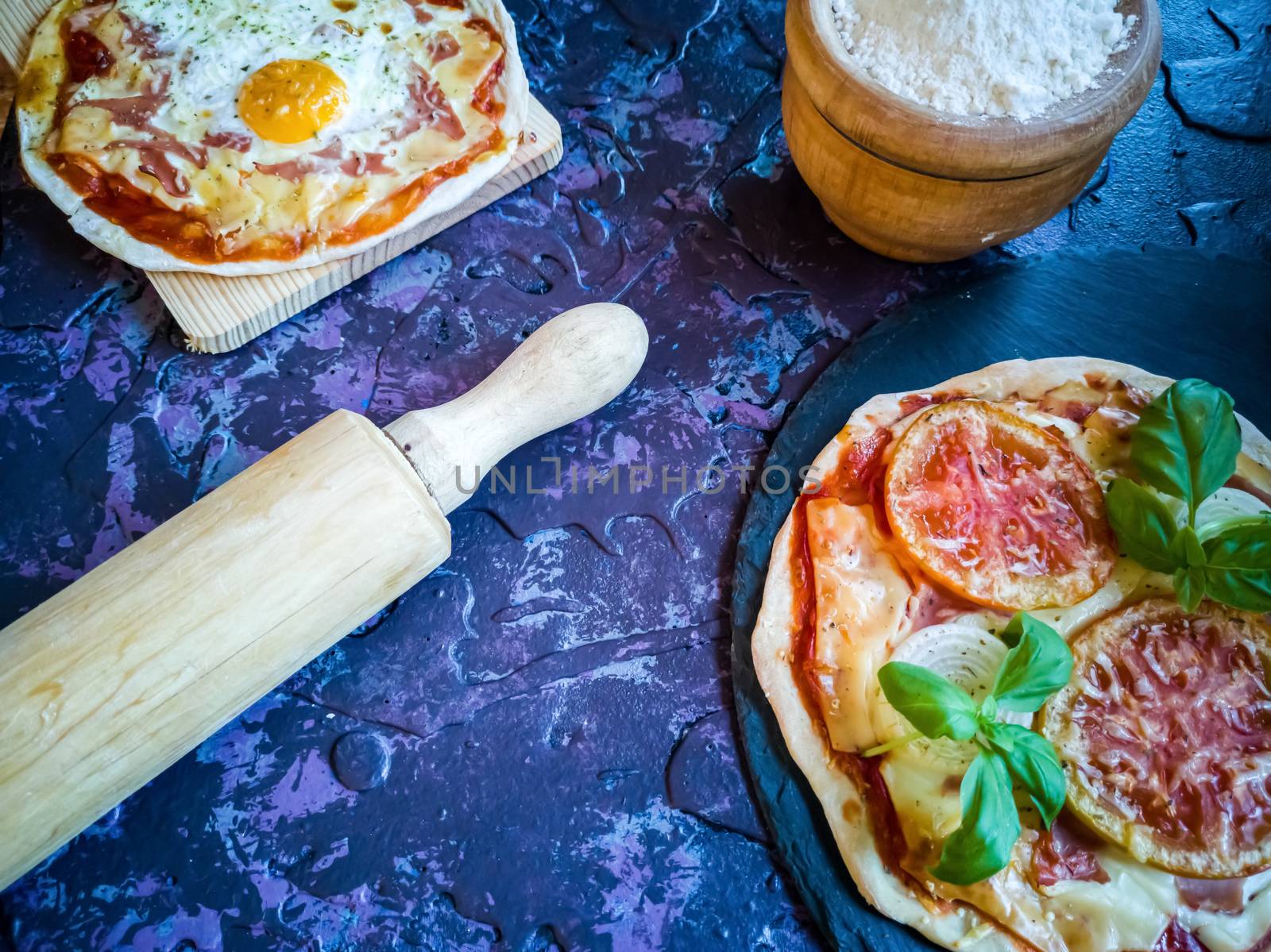 Homemade pizzas and utensils on dark background in lilac tones