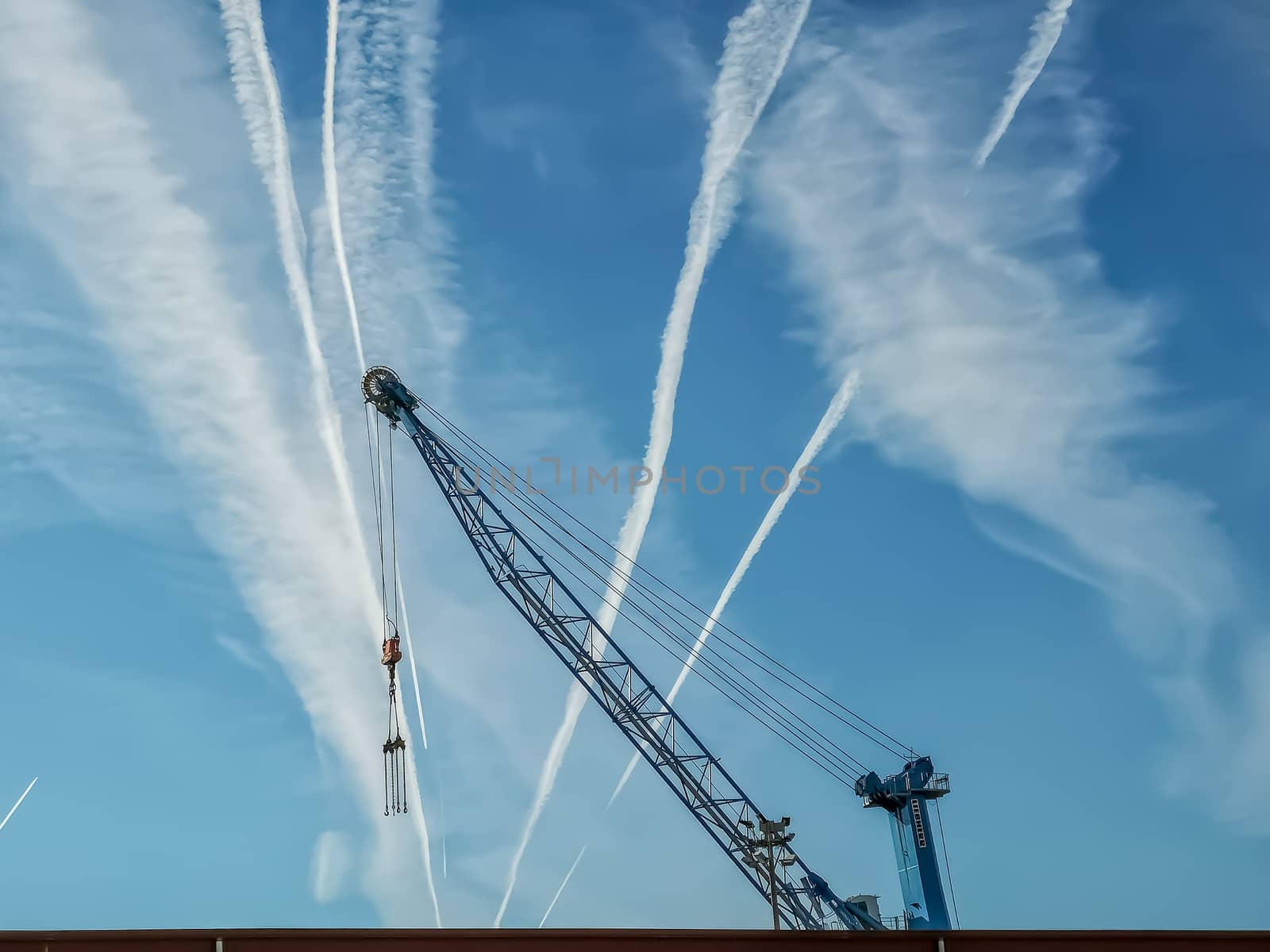 View of blue crane with sky with contrails of aircraft