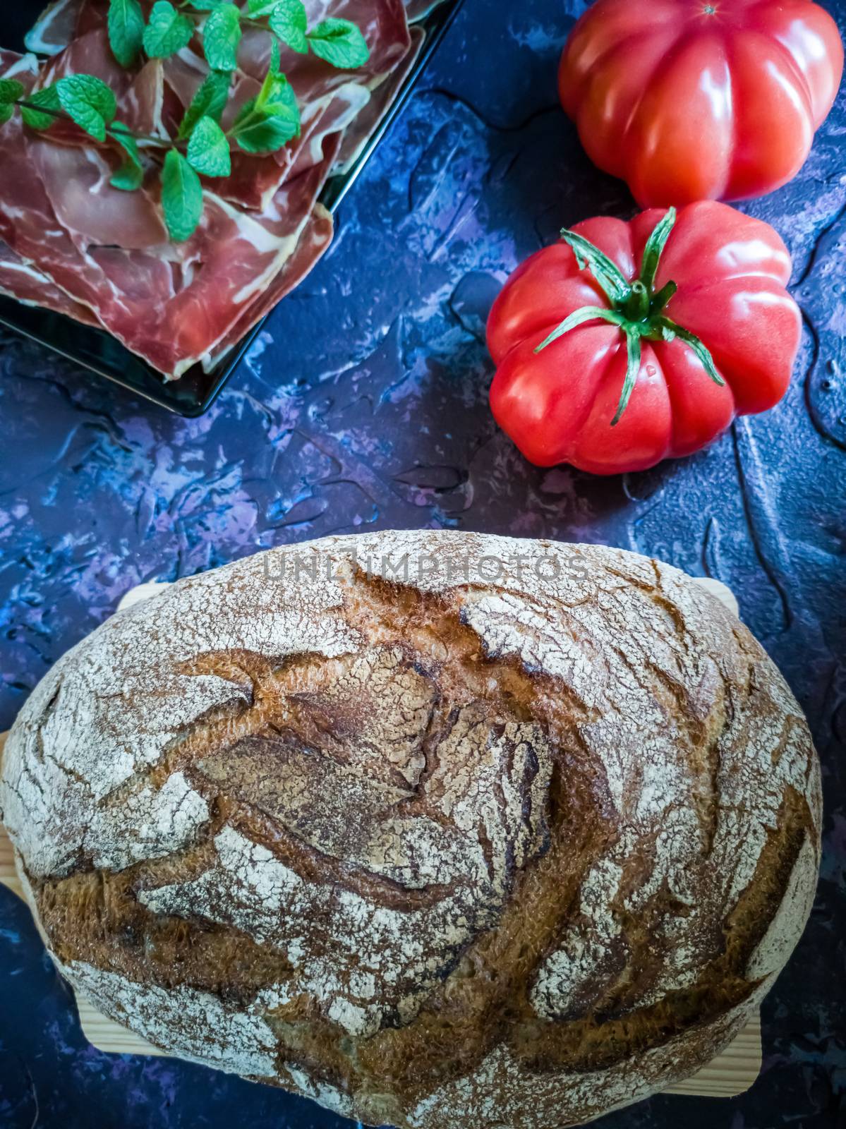 Ham, tomato, bread and herbs in composition on dark background with rough texture