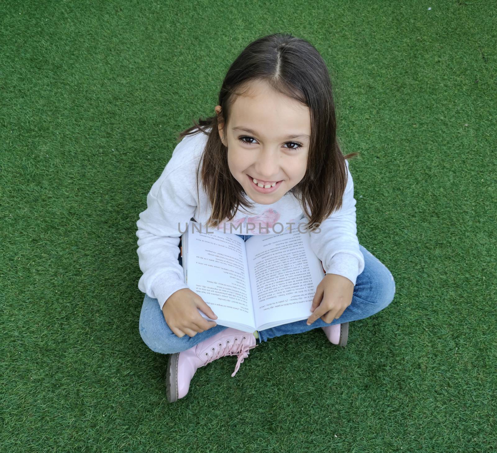 Smiling girl reading sitting on artificial grass