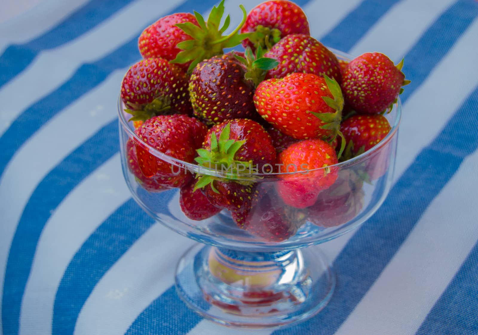 Glass bowl of fresh ripe strawberries on the tablecloth.