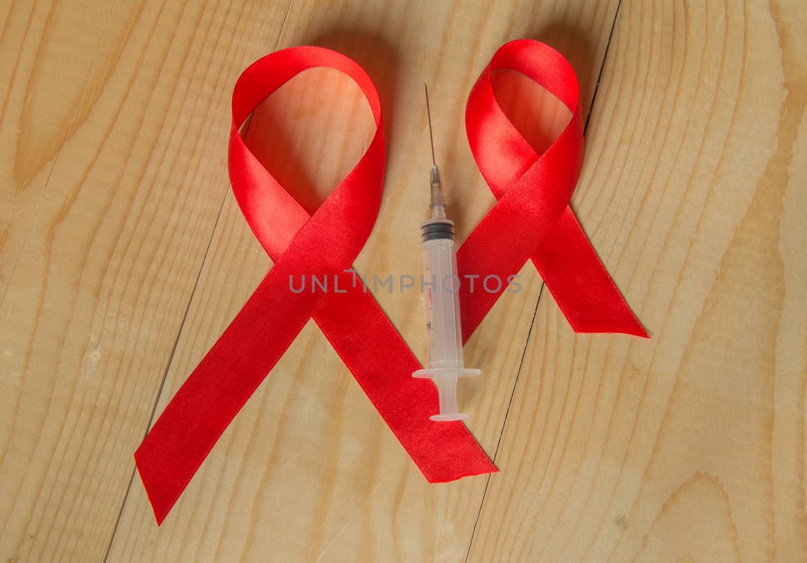 Awareness red ribbon and syringe on wooden background: world day of fight against AIDS, promotion public support for the health people living with HIV in December by claire_lucia