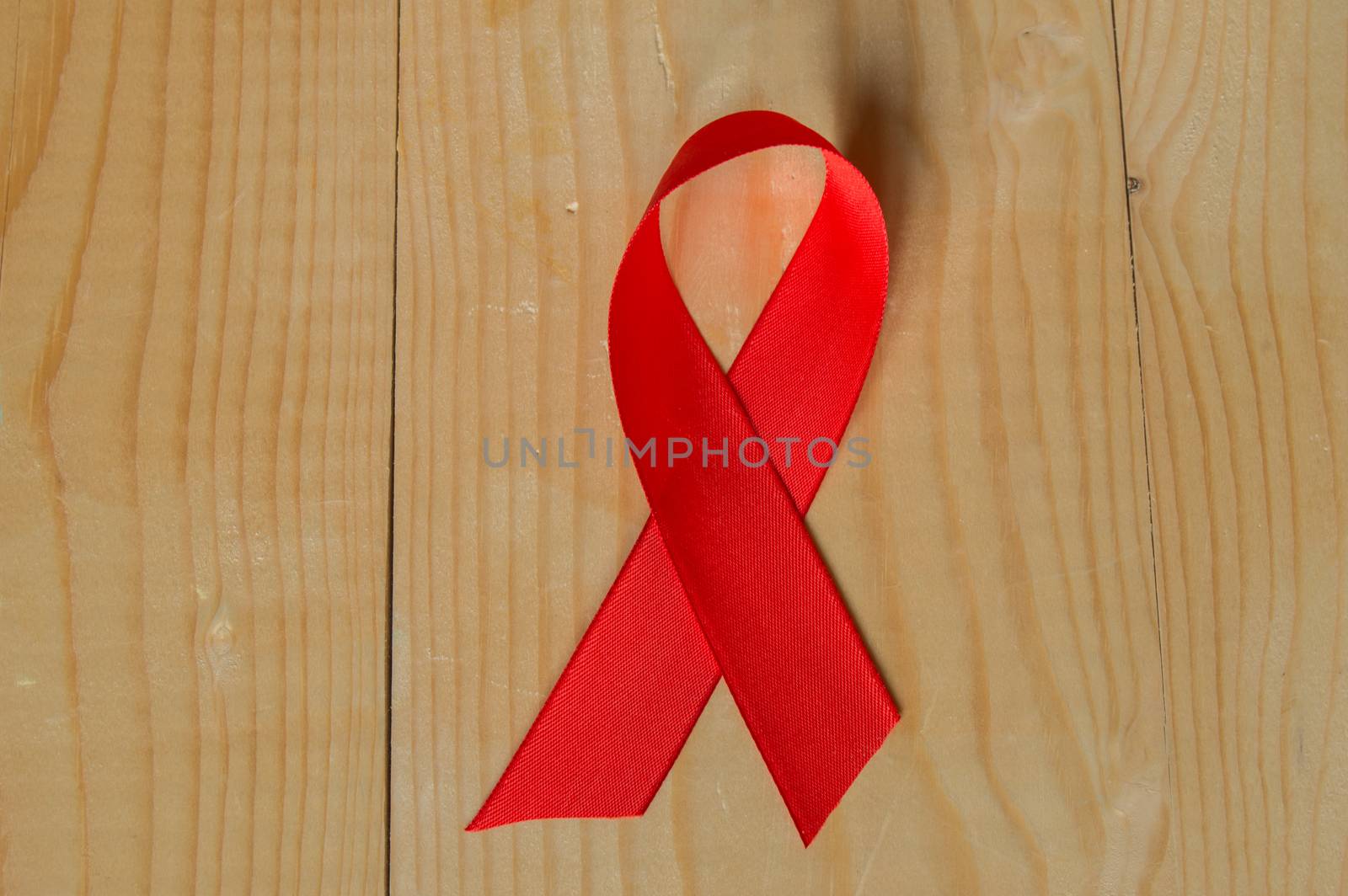 Awareness red ribbon on wood background: world day fight against AIDS, promotions to public support for the health of people living with HIV in December by claire_lucia