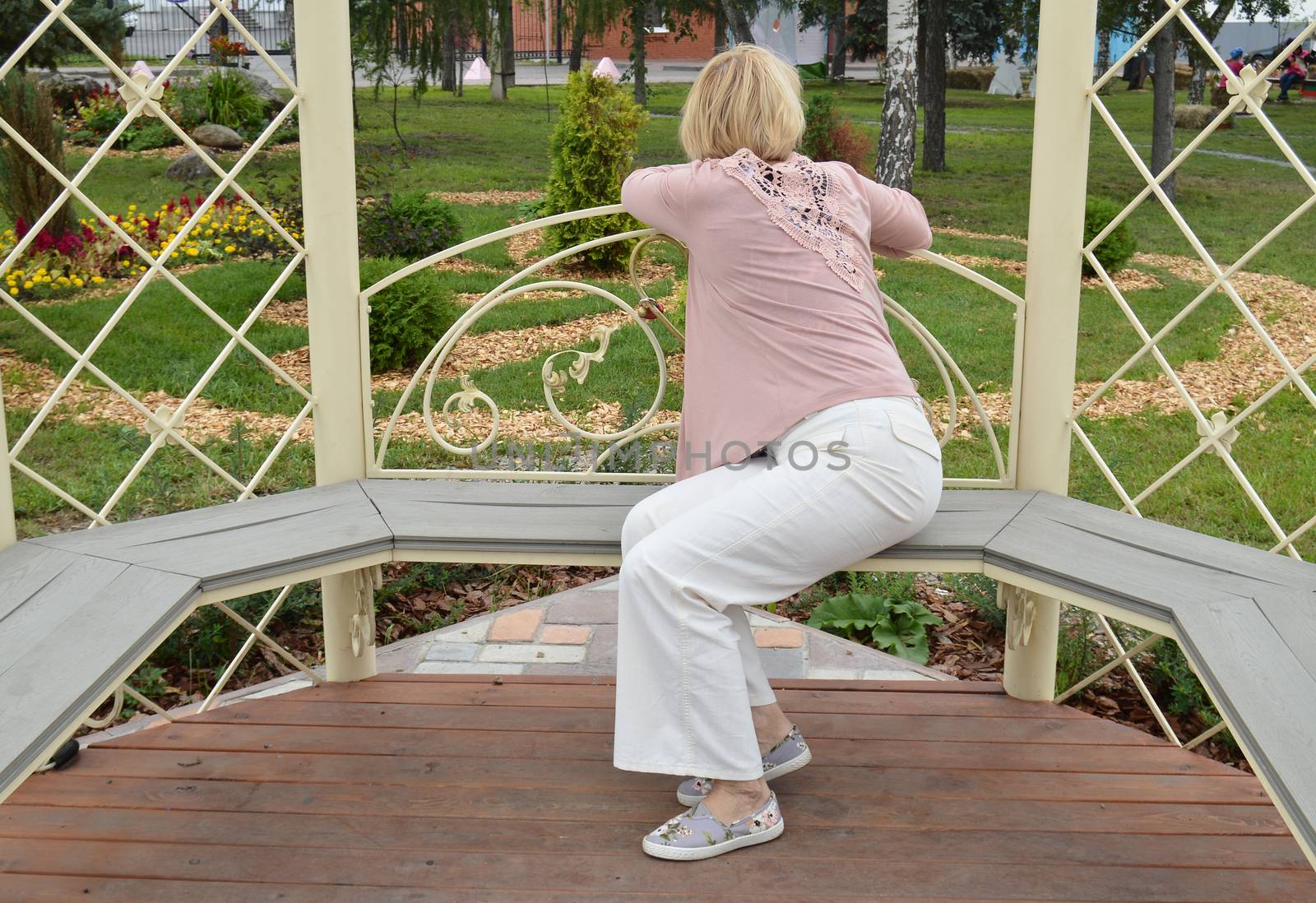 Rear view of young woman sitting and dreaming, leaning on the railing of the wooden gazebo