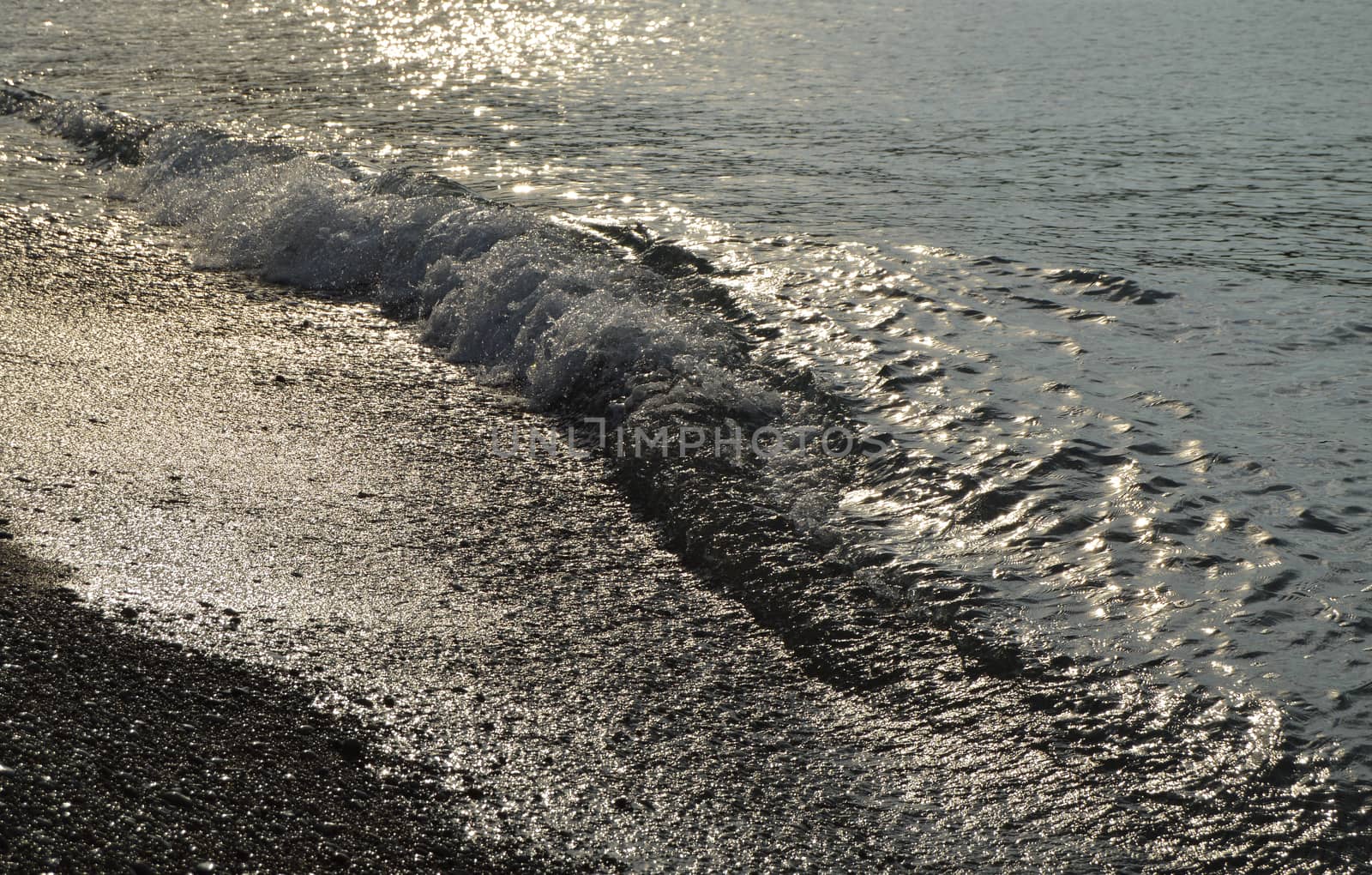 Shiny silver water on the sea pebble beach, early morning sunrise.