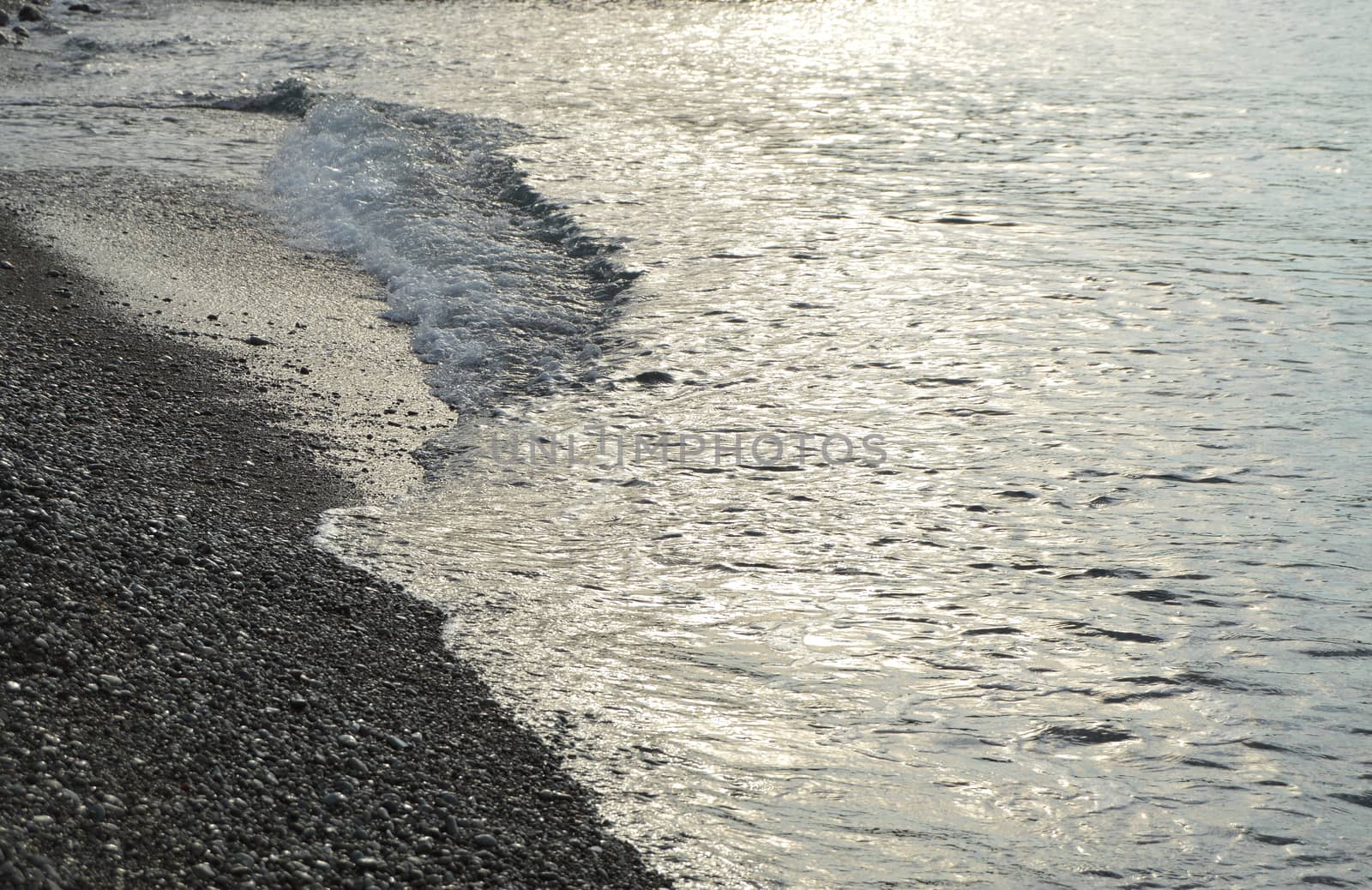 Shiny silver water on the sea pebble beach, early morning sunrise.