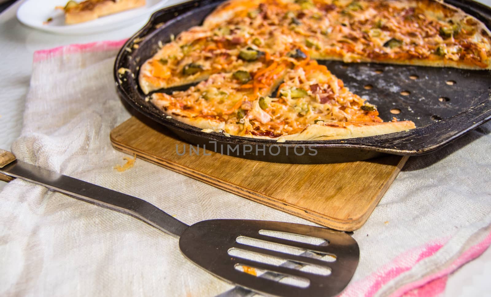 Freshly baked appetizing homemade pizza on a metal pan with cheese and ham, close-up selective focus.